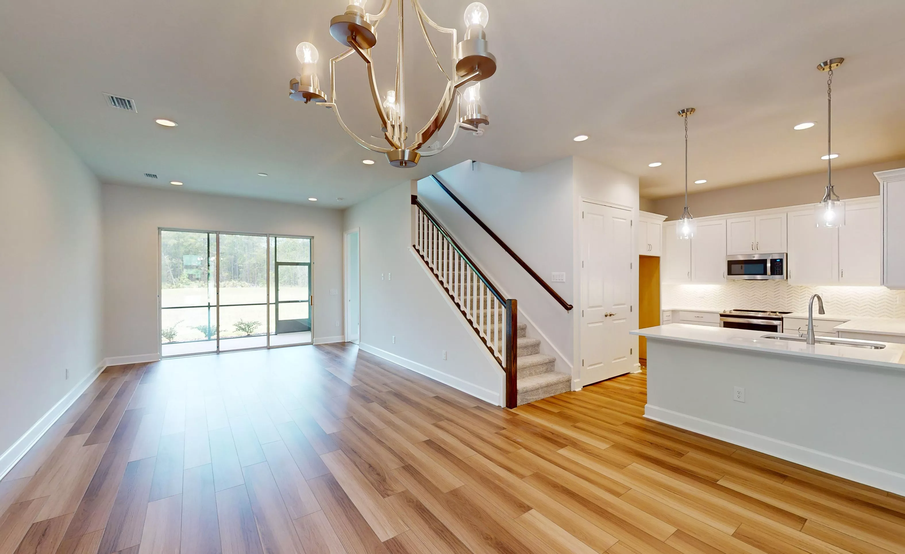 Blossom II living room with wood-look flooring, staircase with white railing, chandelier, and adjacent open kitchen.