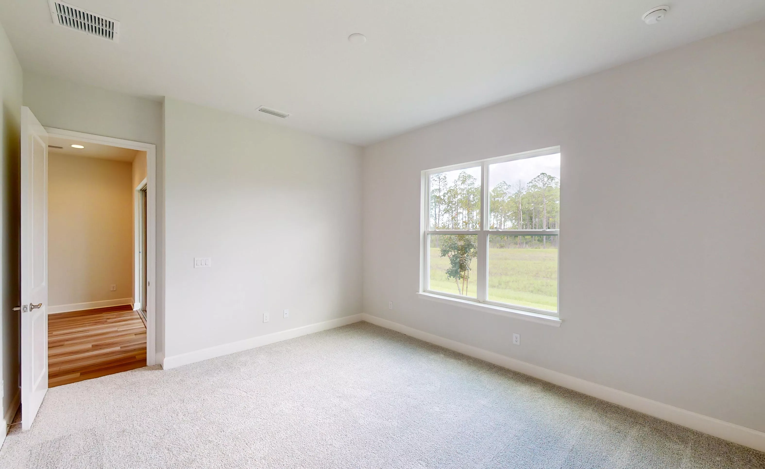 Empty secondary bedroom in the Blossom II plan with light gray carpet, off-white walls, and a window view of trees.