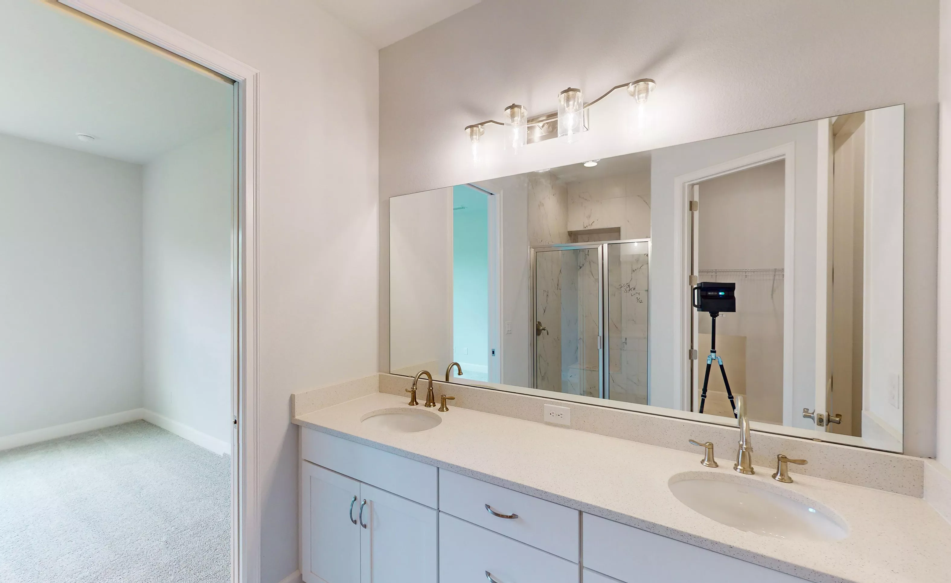 Blossom II secondary bath with dual-sink vanity, light countertops, gold fixtures, and a large wall-to-wall mirror.