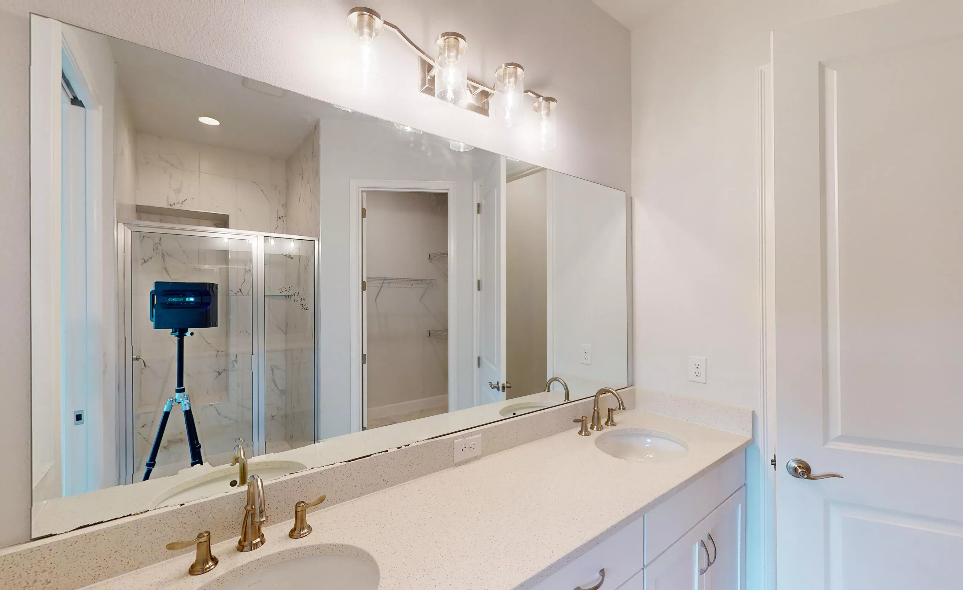 Primary bath in Blossom II plan with double vanity, light-colored countertops, gold fixtures, and a walk-in shower.
