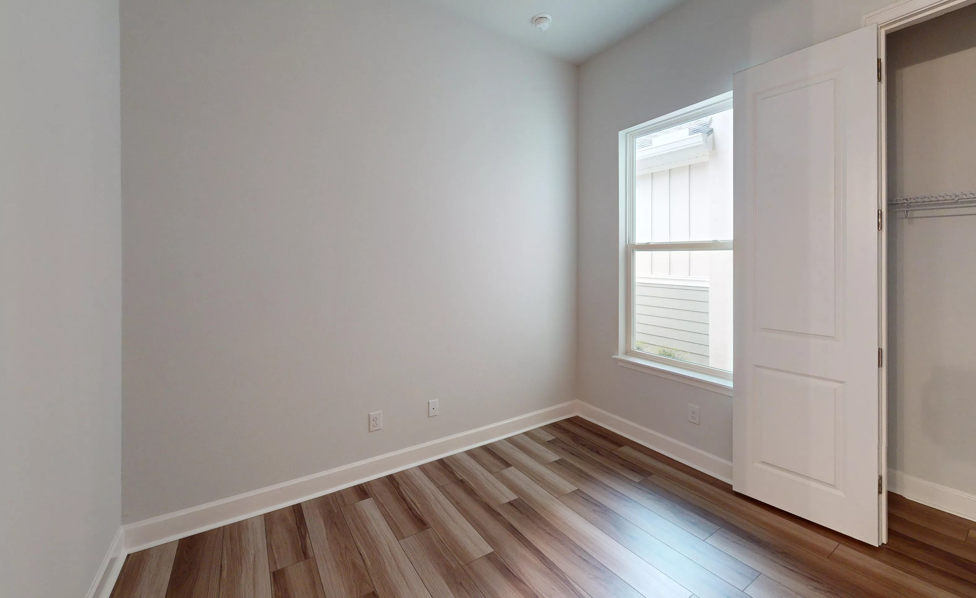 Secondary bedroom with gray walls, wood-look plank flooring, a single window, and an open closet door.
