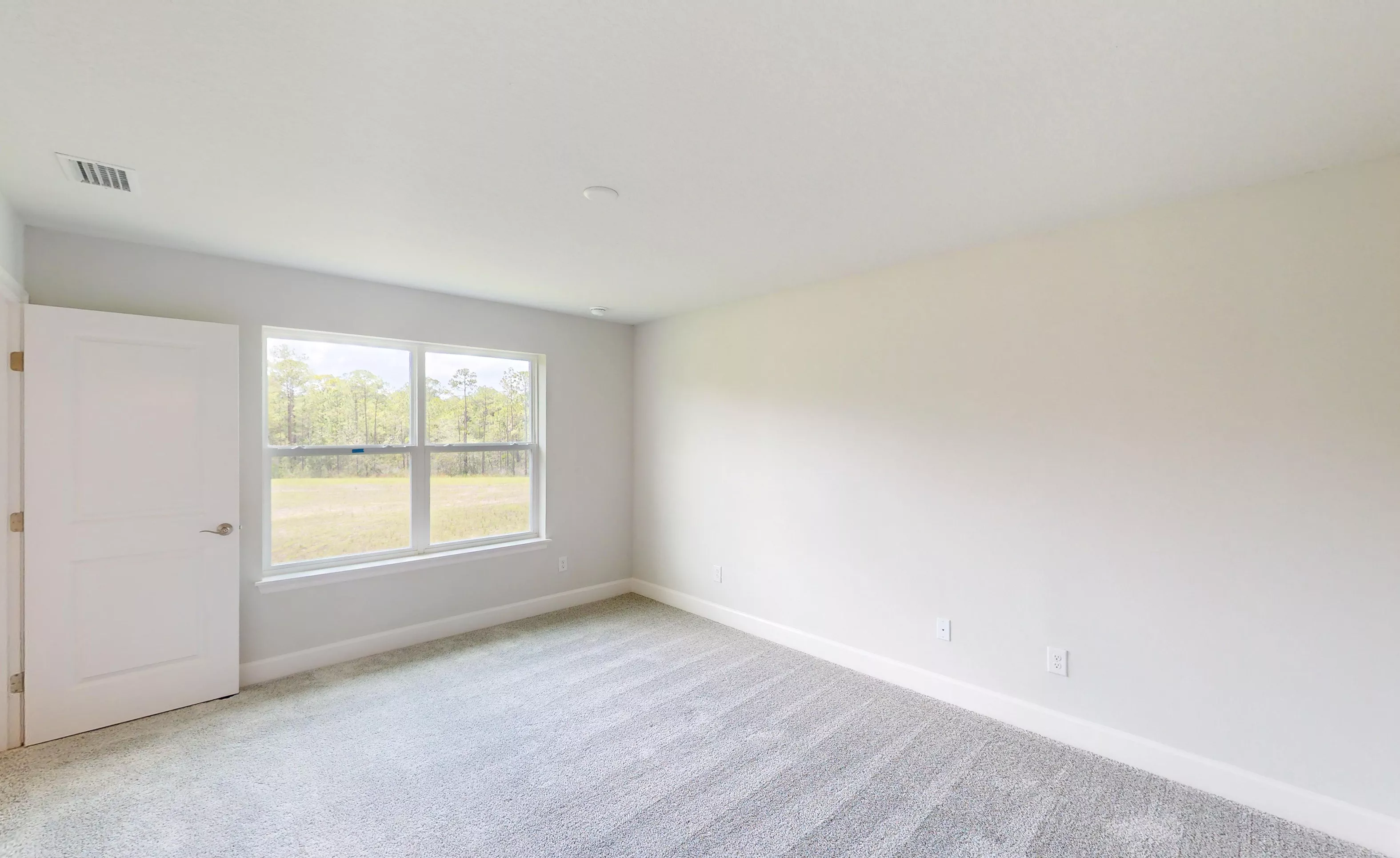 Empty secondary bedroom in the Blossom II plan with light gray carpet, white walls, and a window overlooking a grassy lot.