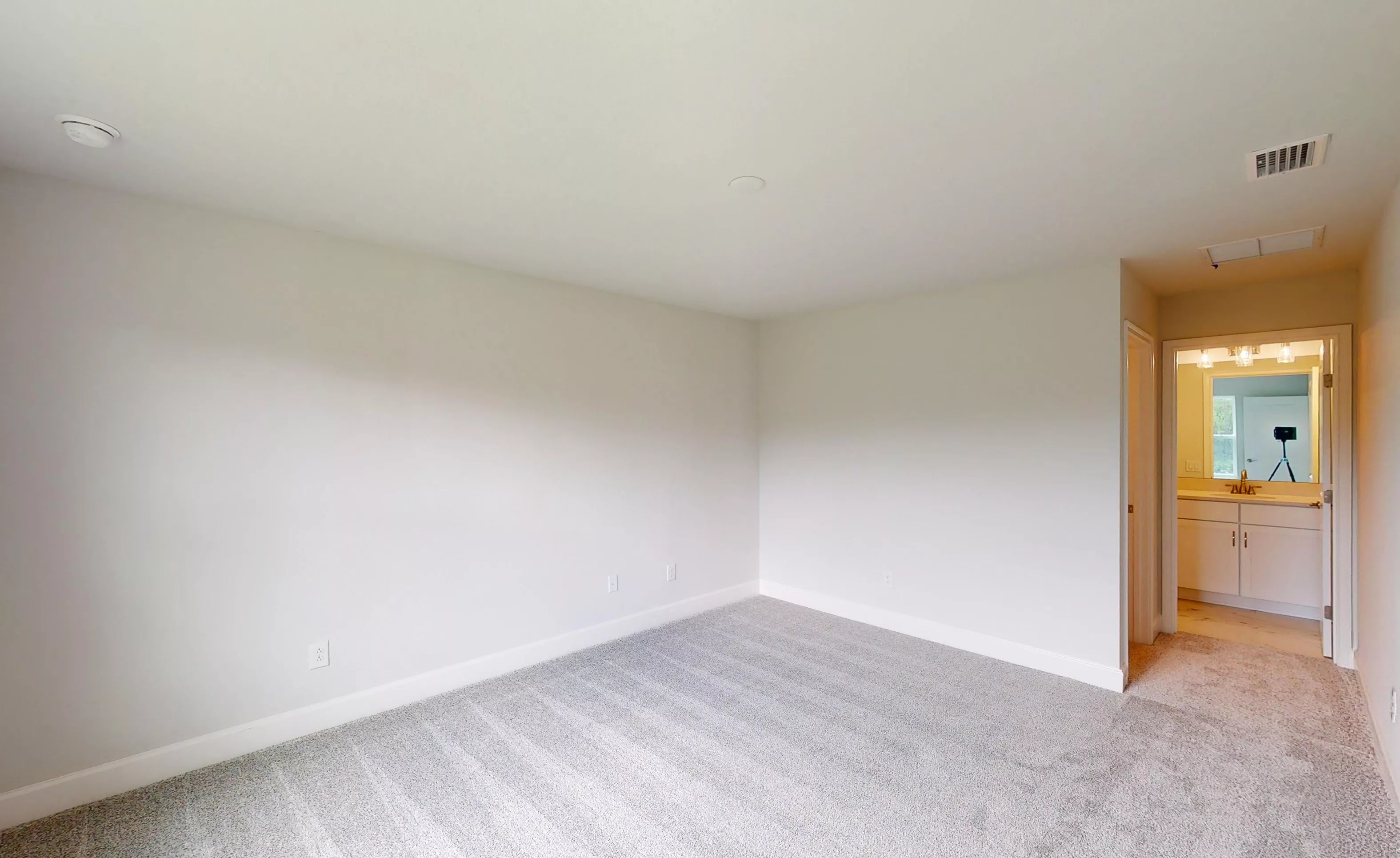Empty secondary bedroom with neutral walls, carpeted floors, and a doorway leading to an adjoining bathroom.