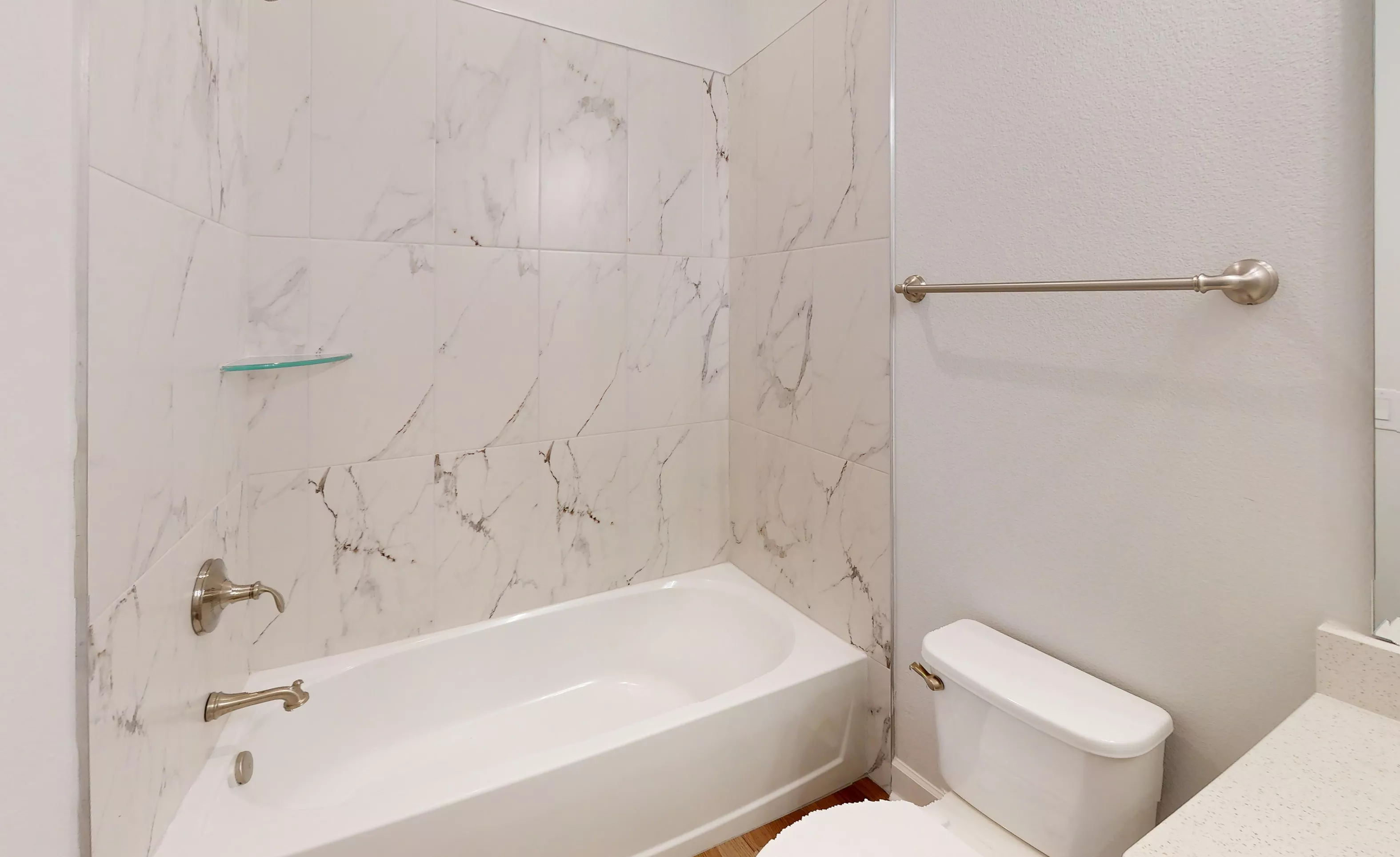 Secondary bath in Blossom II plan with white tub, white marble-look wall tiles, chrome fixtures, and a white toilet.