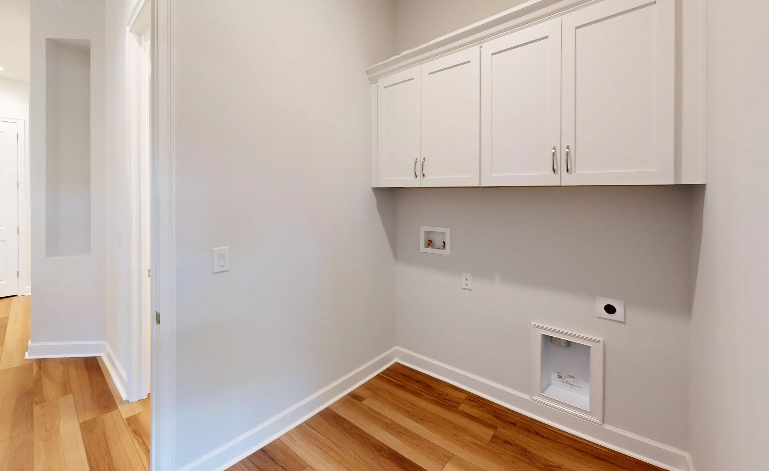 Laundry room with white upper cabinets, light gray walls, and wood-look flooring.