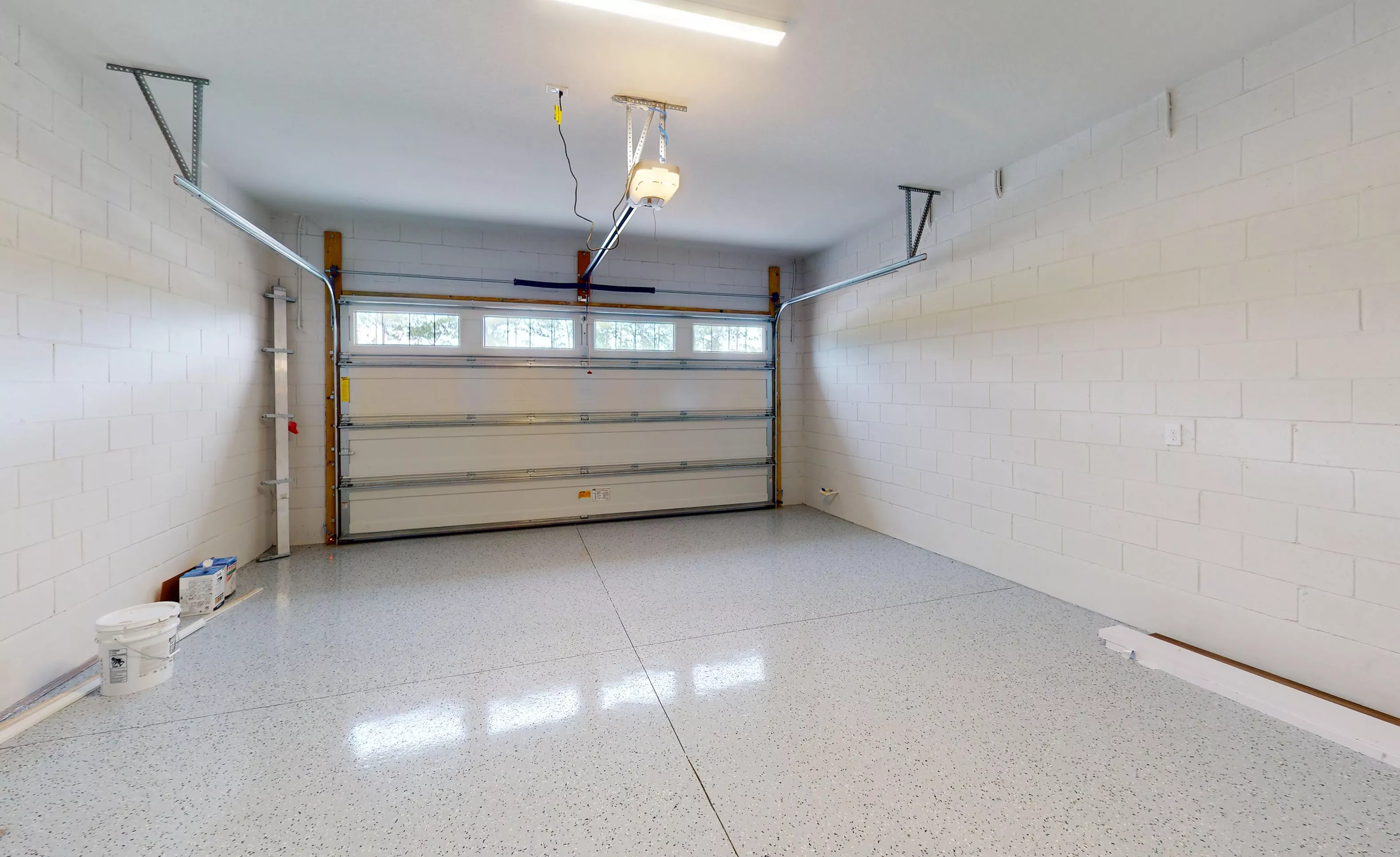 Empty garage in the Blossom II plan with white painted block walls, a glossy speckled floor, and a sectional door.