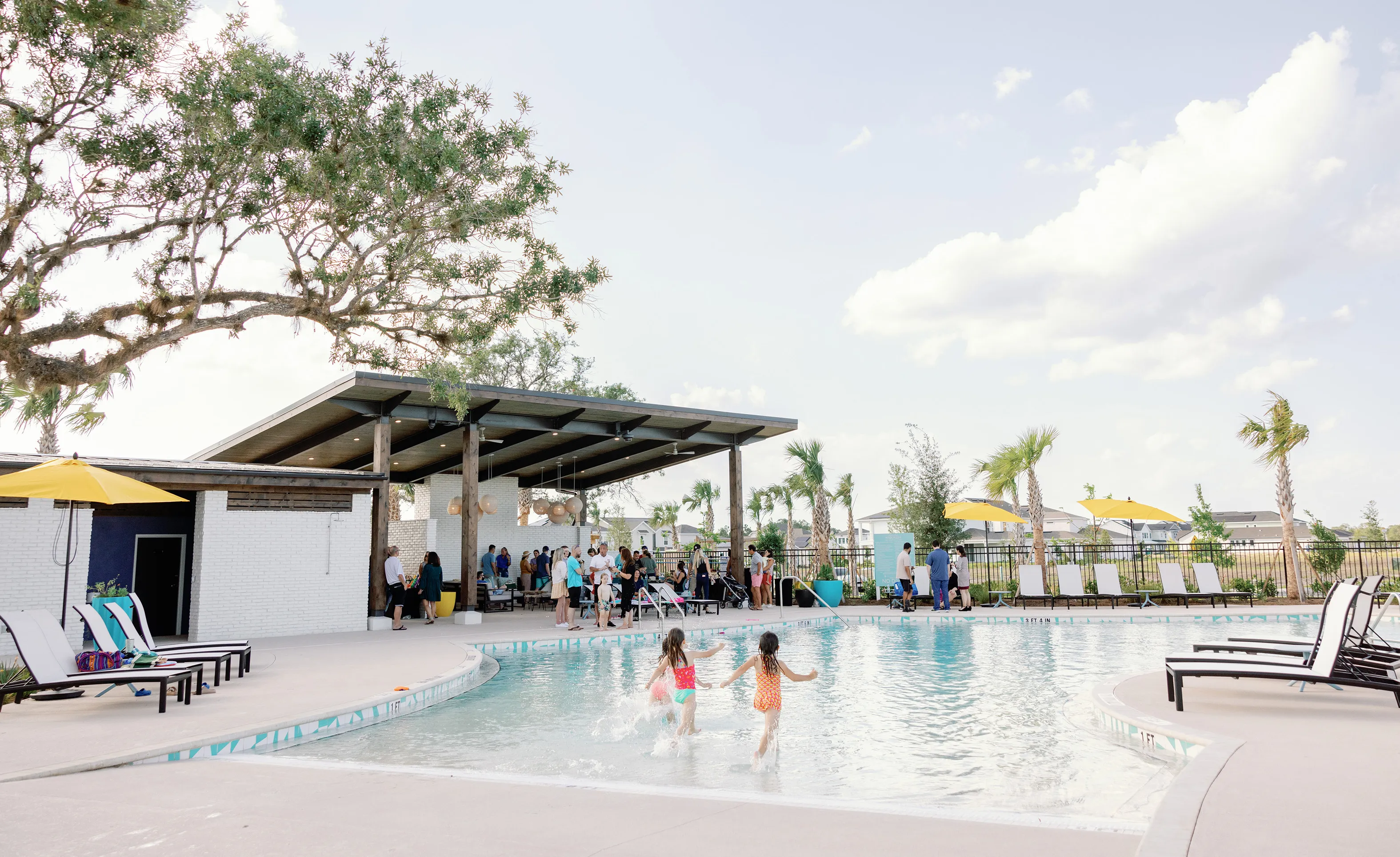 People gathering at the Weslyn Park at Sunbridge community pool, which features a covered pavilion, lounge chairs, and kids.