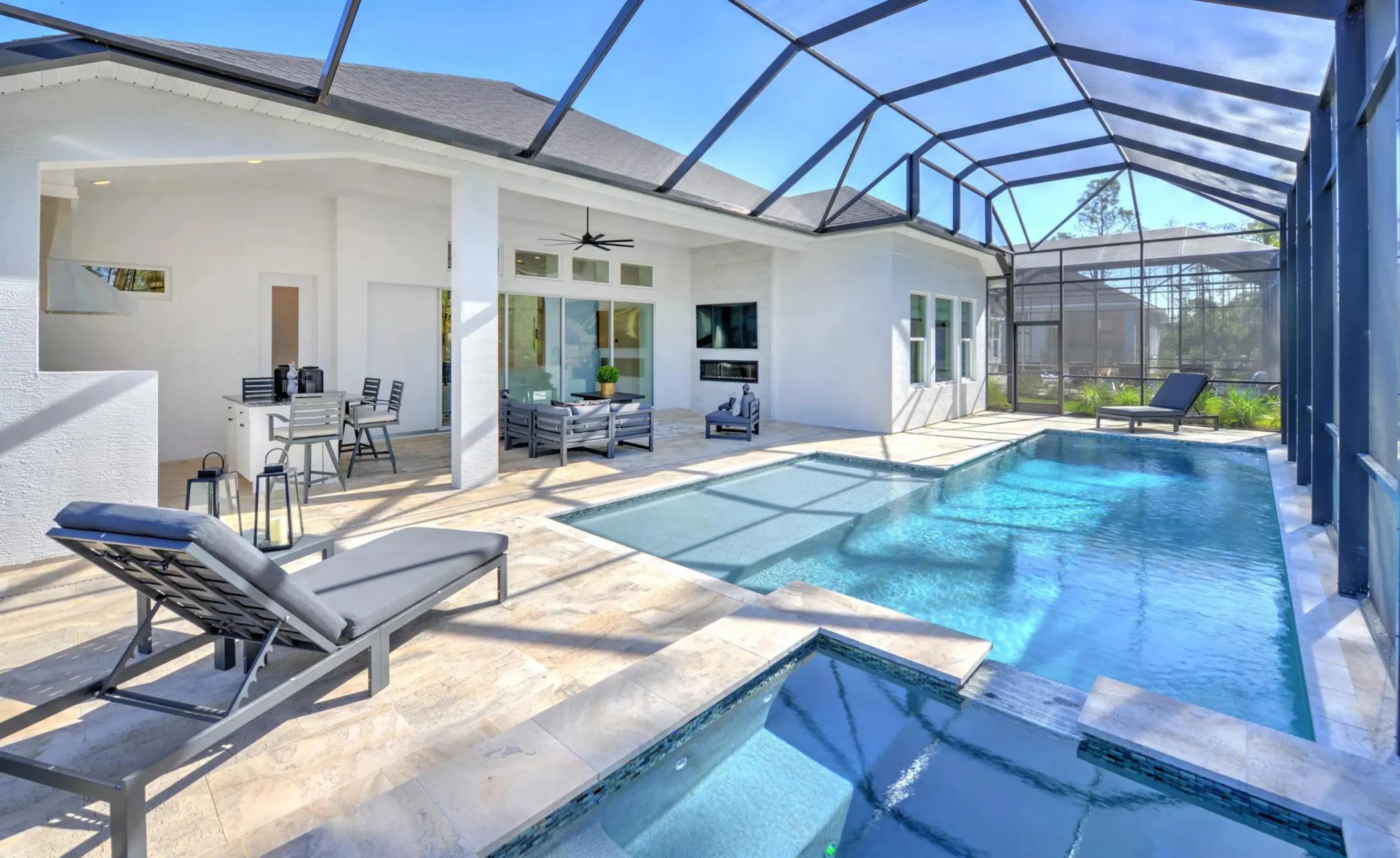 Screened-in patio in Woodhaven with a pool, spa, outdoor dining area, fireplace, and lounge chairs on stone pavers.