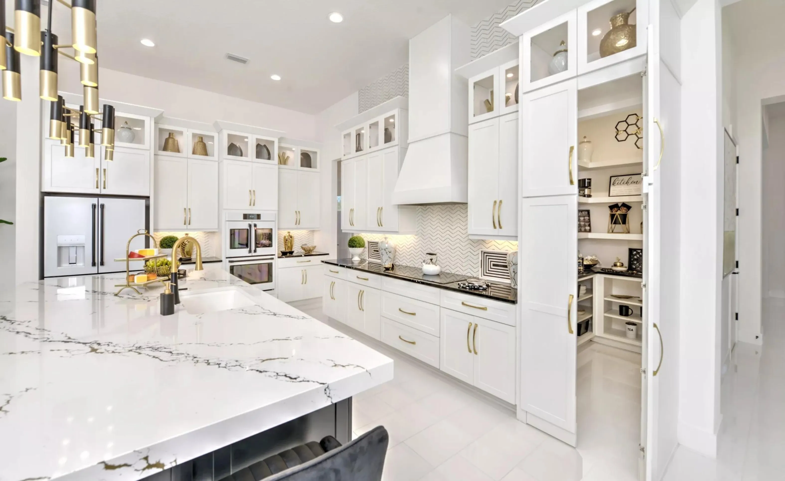 White kitchen in Woodhaven with a marble-topped island, gold hardware, chevron tile backsplash, and a walk-in pantry.