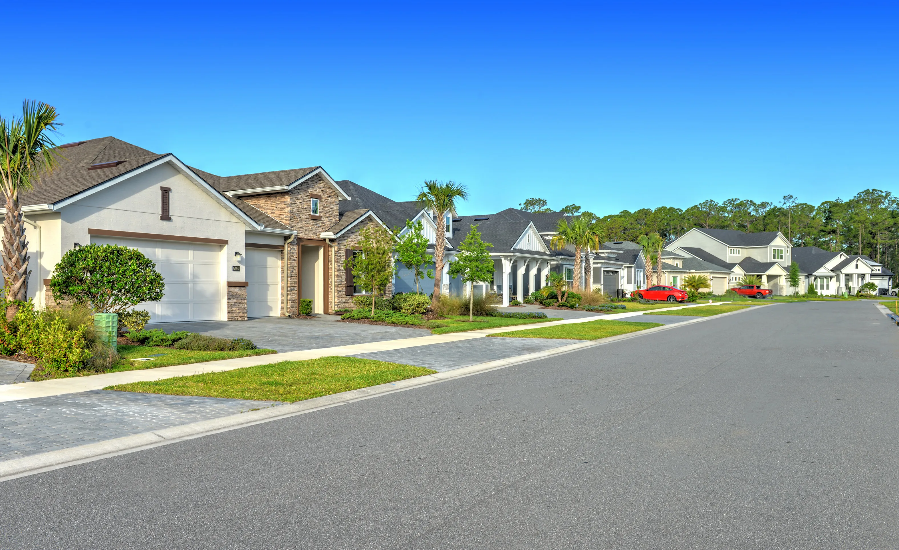 Street view of modern single-family homes in the Woodhaven community with paver driveways and manicured landscaping.