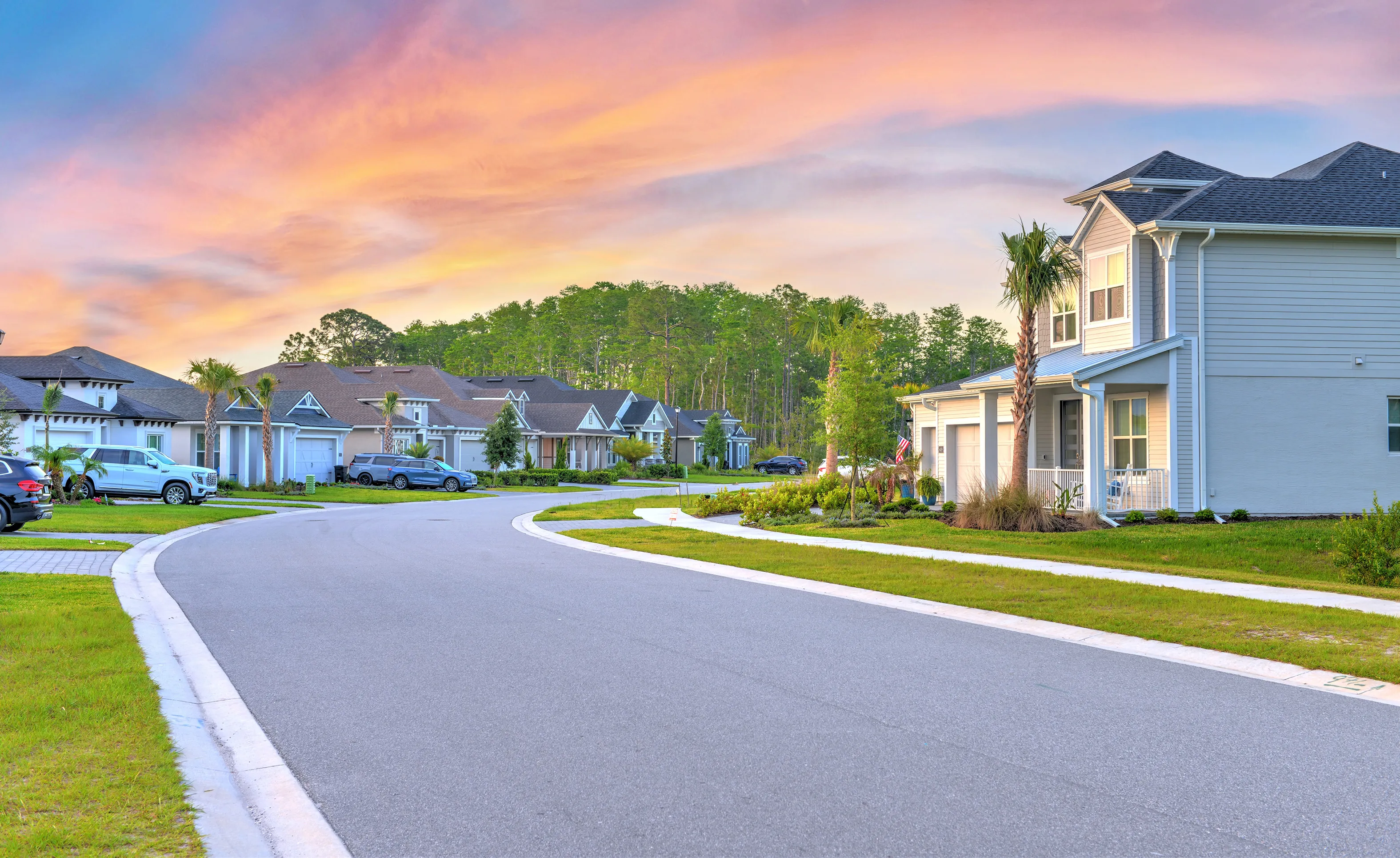 A winding street in the Woodhaven community lined with modern single-family homes under a sunset sky.