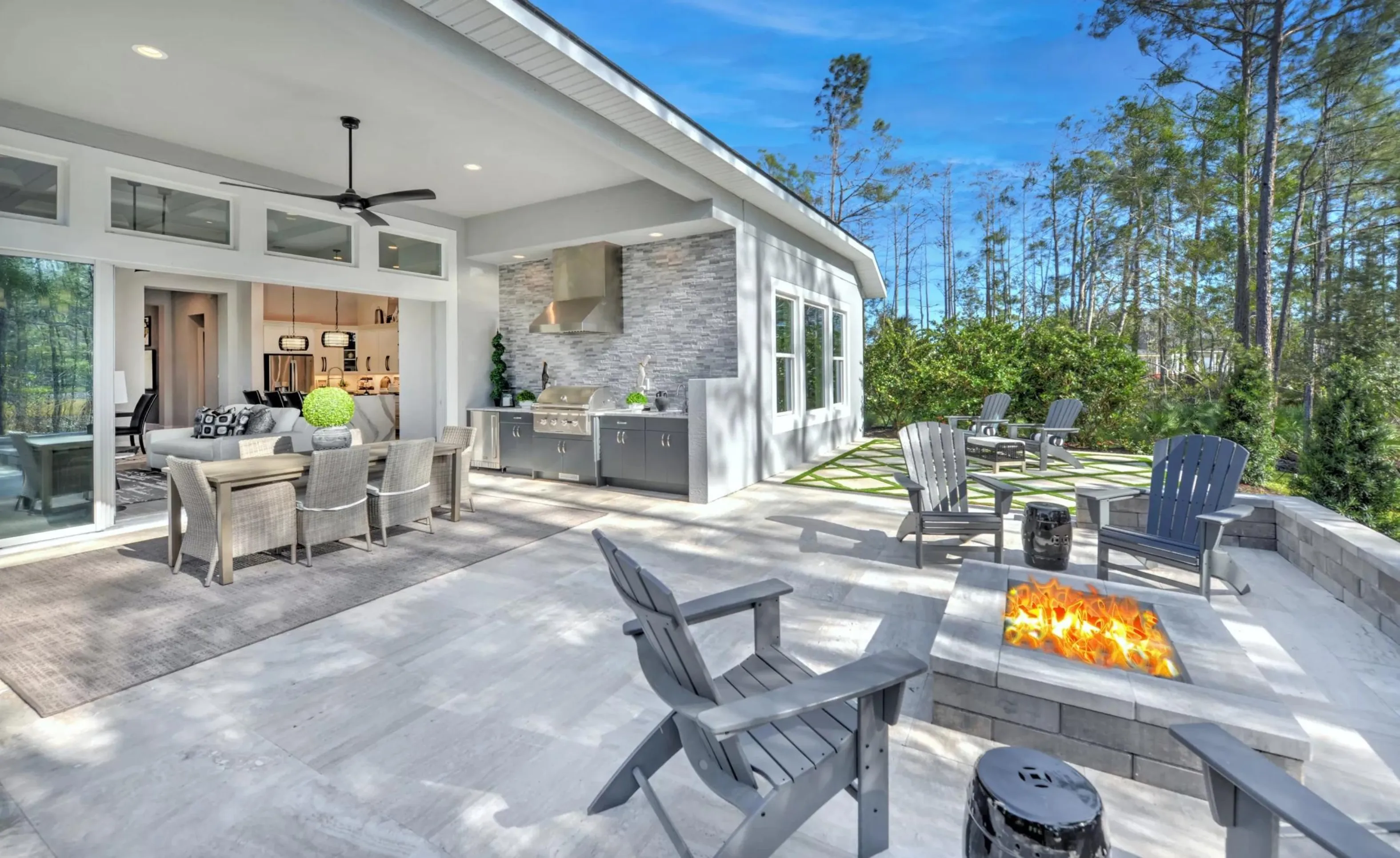 Covered patio at Woodhaven featuring an outdoor kitchen, dining set, fire pit with Adirondack chairs, and stone flooring.
