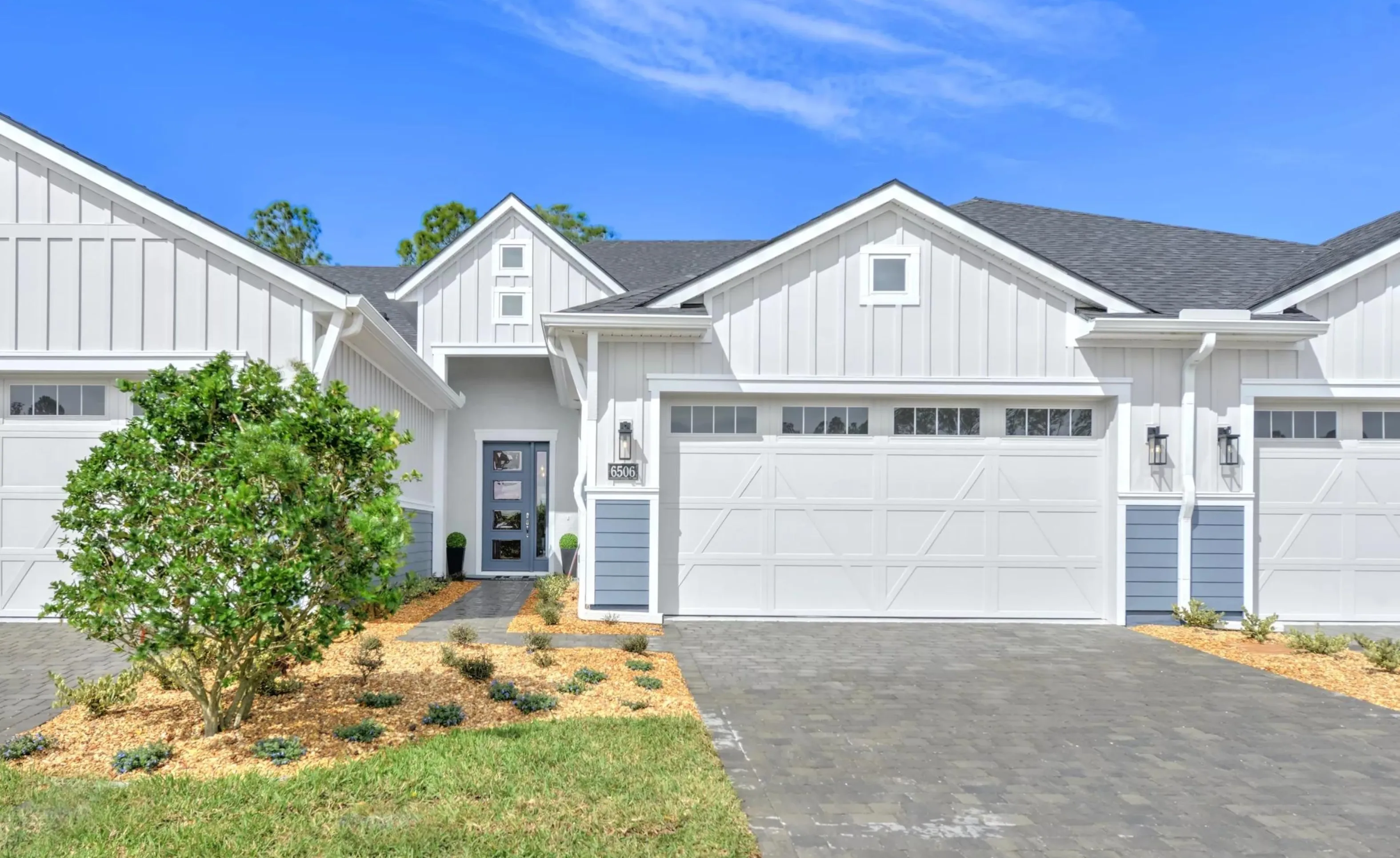 Exterior view of a Woodhaven model home with white vertical siding, blue accents, a gray paver driveway, and front door.