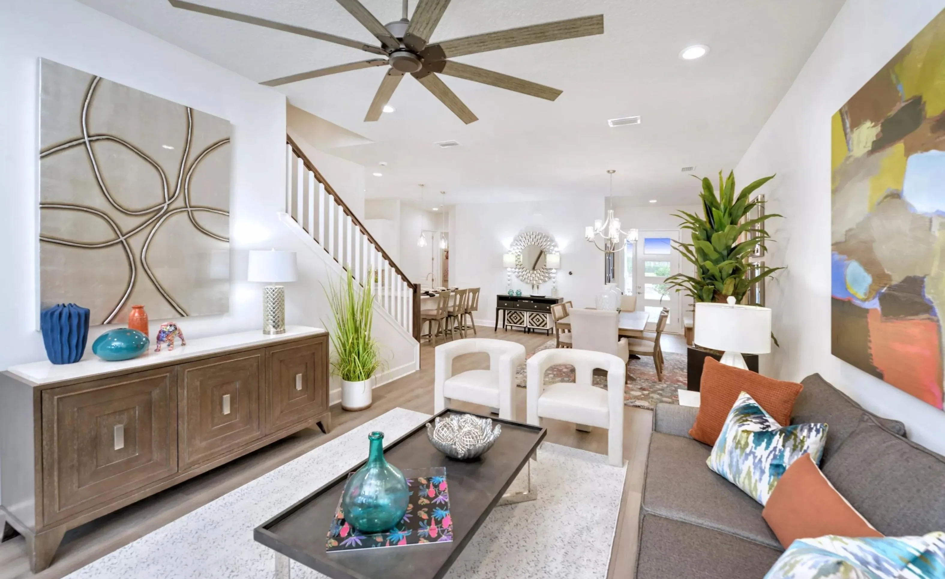 Open living area at Woodhaven with a staircase, modern ceiling fan, living room furniture, and dining area in the back.