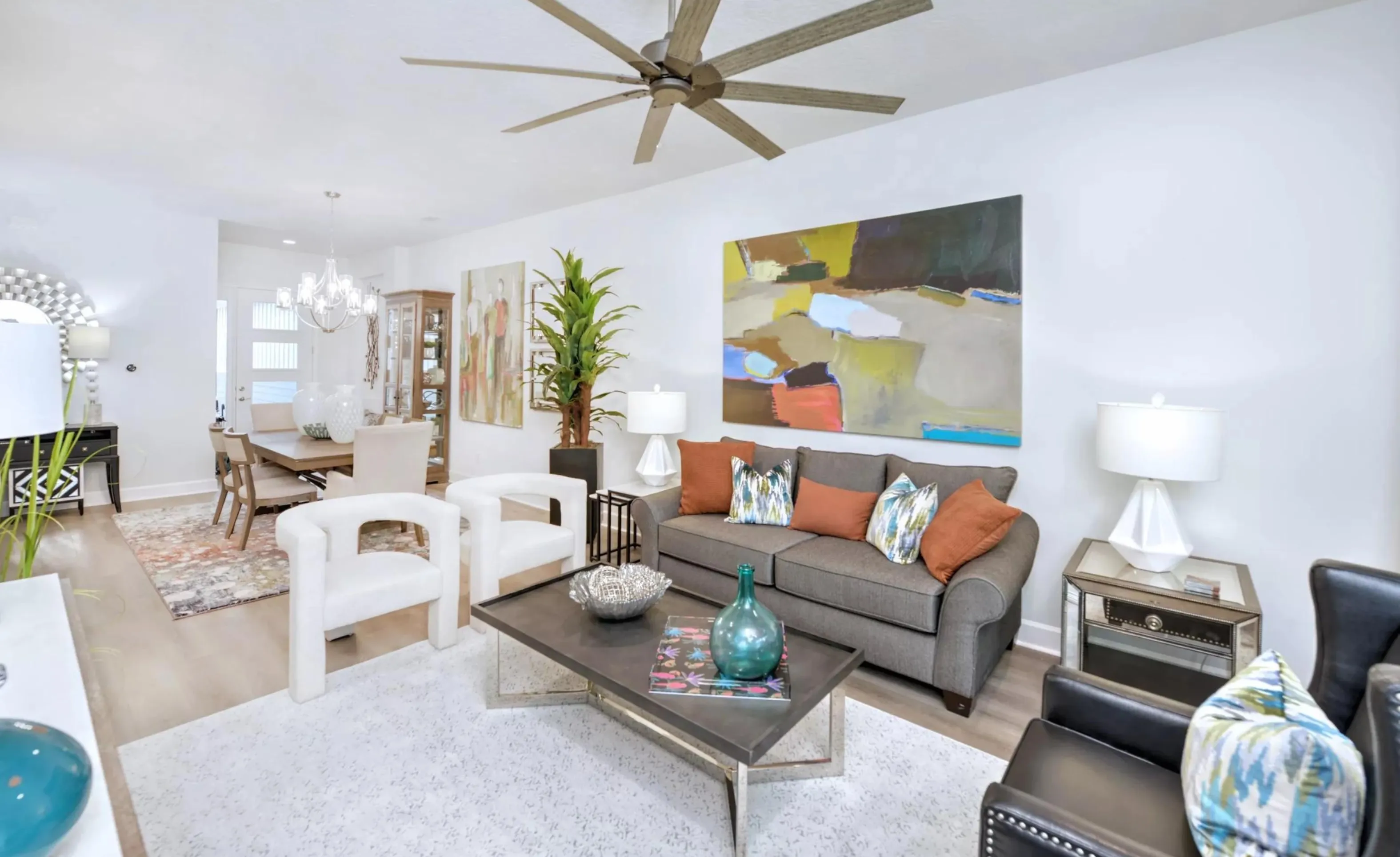 Living room and dining area in Woodhaven, featuring neutral decor, a gray sofa, white armchairs, and a large wall painting.