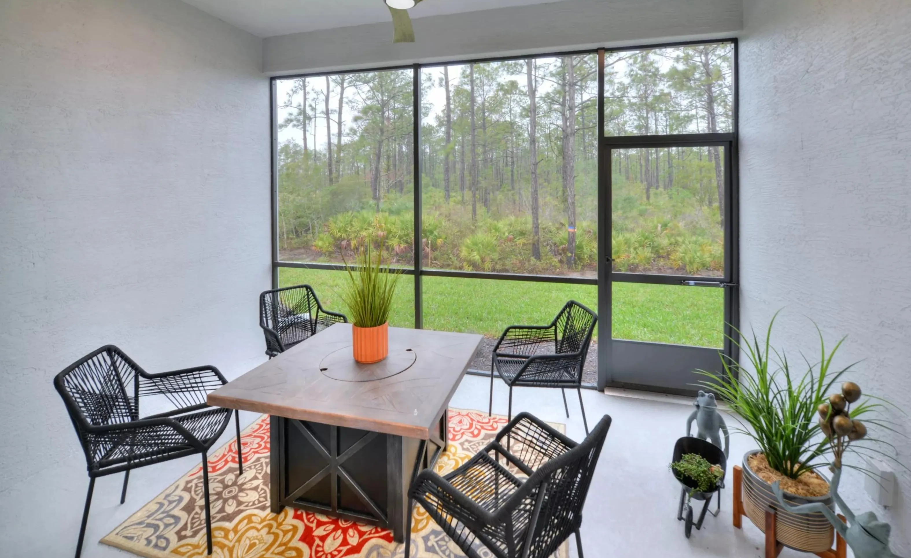 Screened-in patio in Woodhaven with a dark wood table, four black chairs, and a patterned rug overlooking a wooded area.