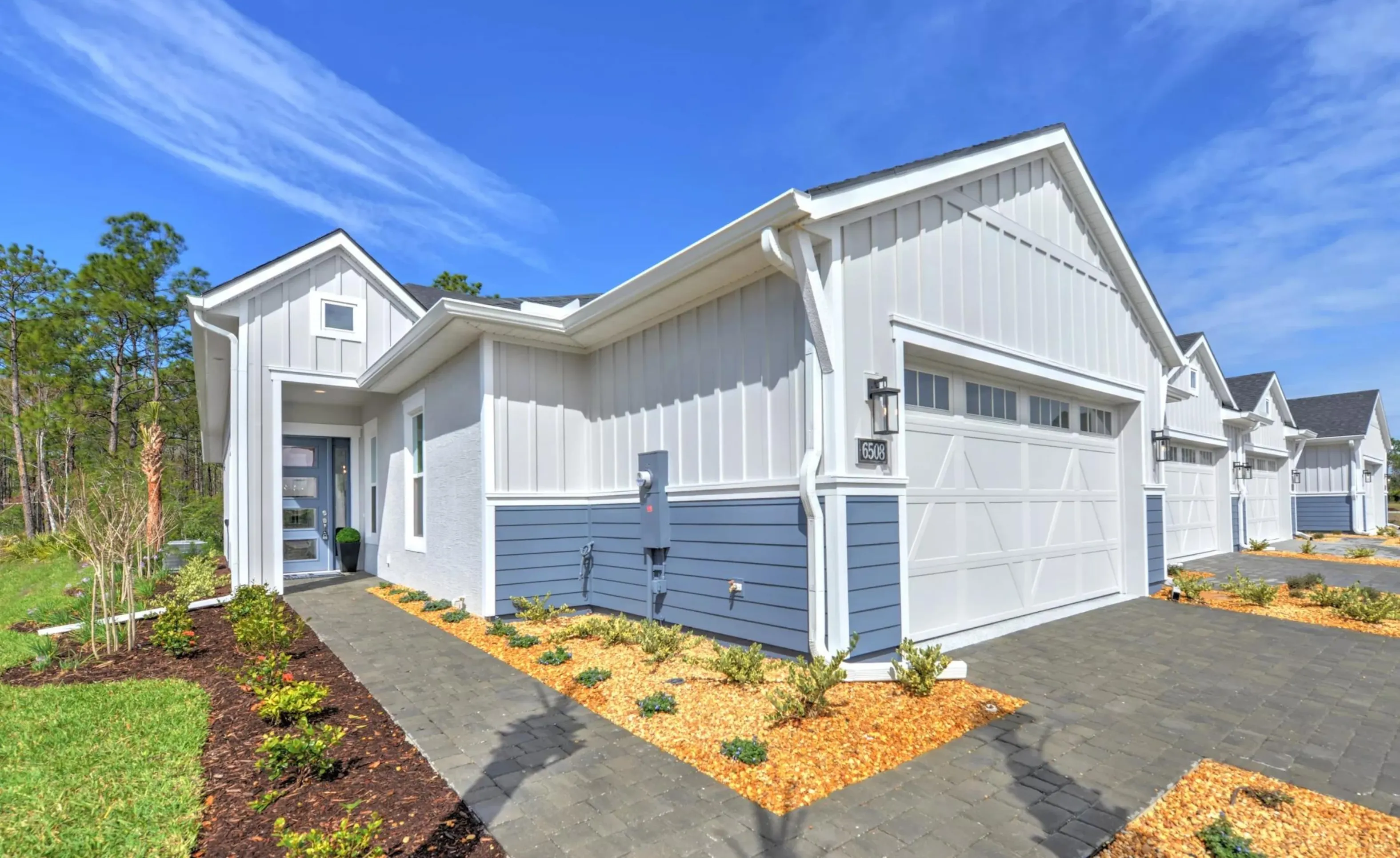 Exterior of a Woodhaven model home featuring white board-and-batten siding, blue lap siding, and a white garage door.