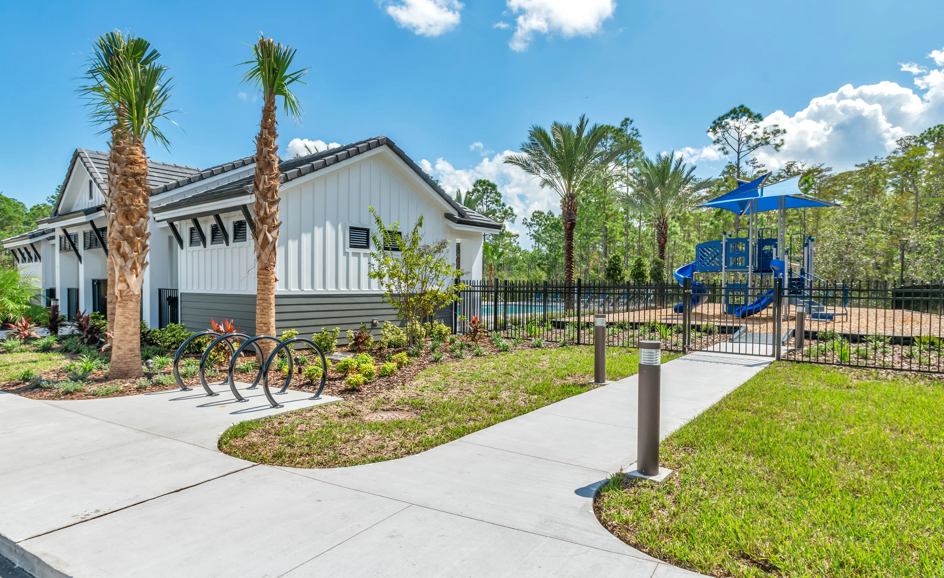 Outdoor community amenity area in Woodhaven featuring a white building, palm trees, a bike rack, and a playground.