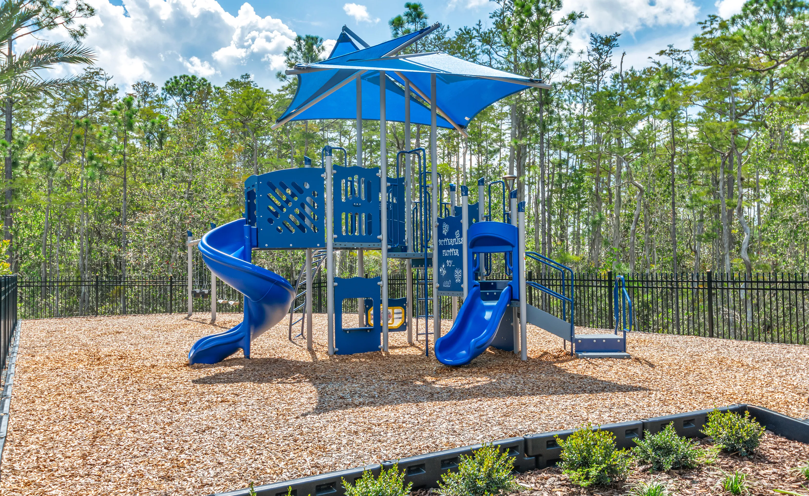 Blue playground structure with slides and a canopy on a wood-chip surface in the Woodhaven community.