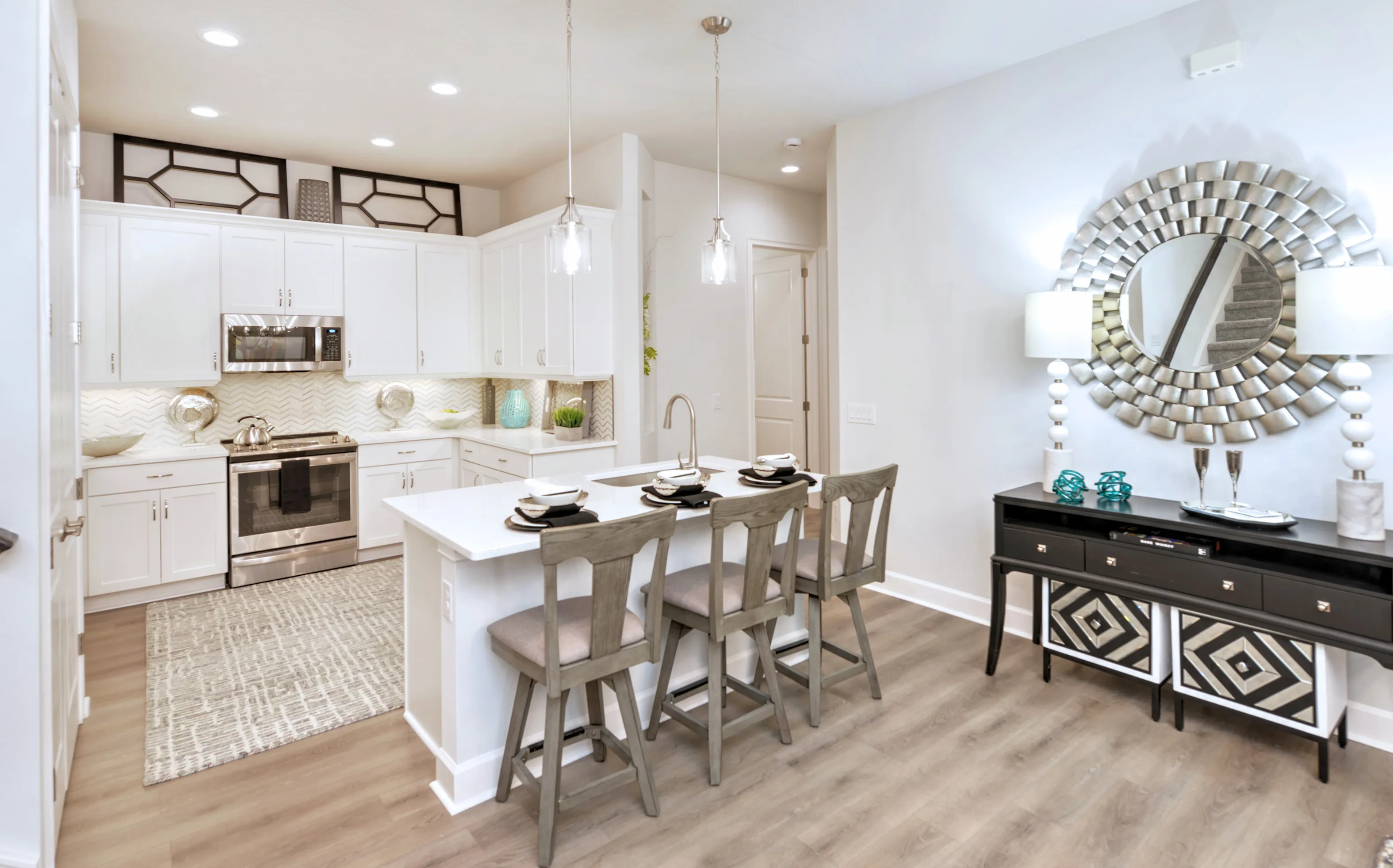 Kitchen in a Woodhaven Townhome featuring white cabinets, an island with three barstools, and a black sideboard with a mirror.