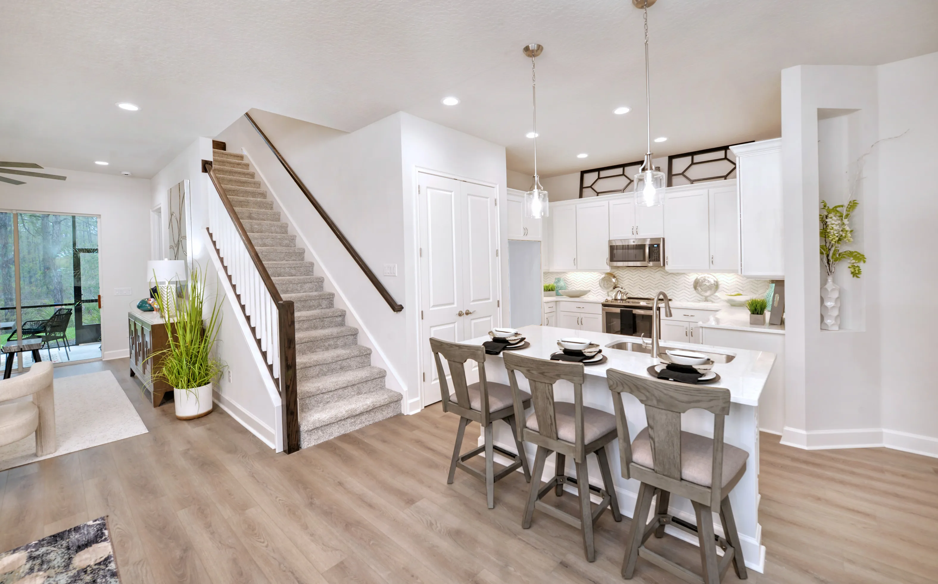 Woodhaven Townhomes kitchen featuring white cabinets, a kitchen island with three stools, and a carpeted staircase.