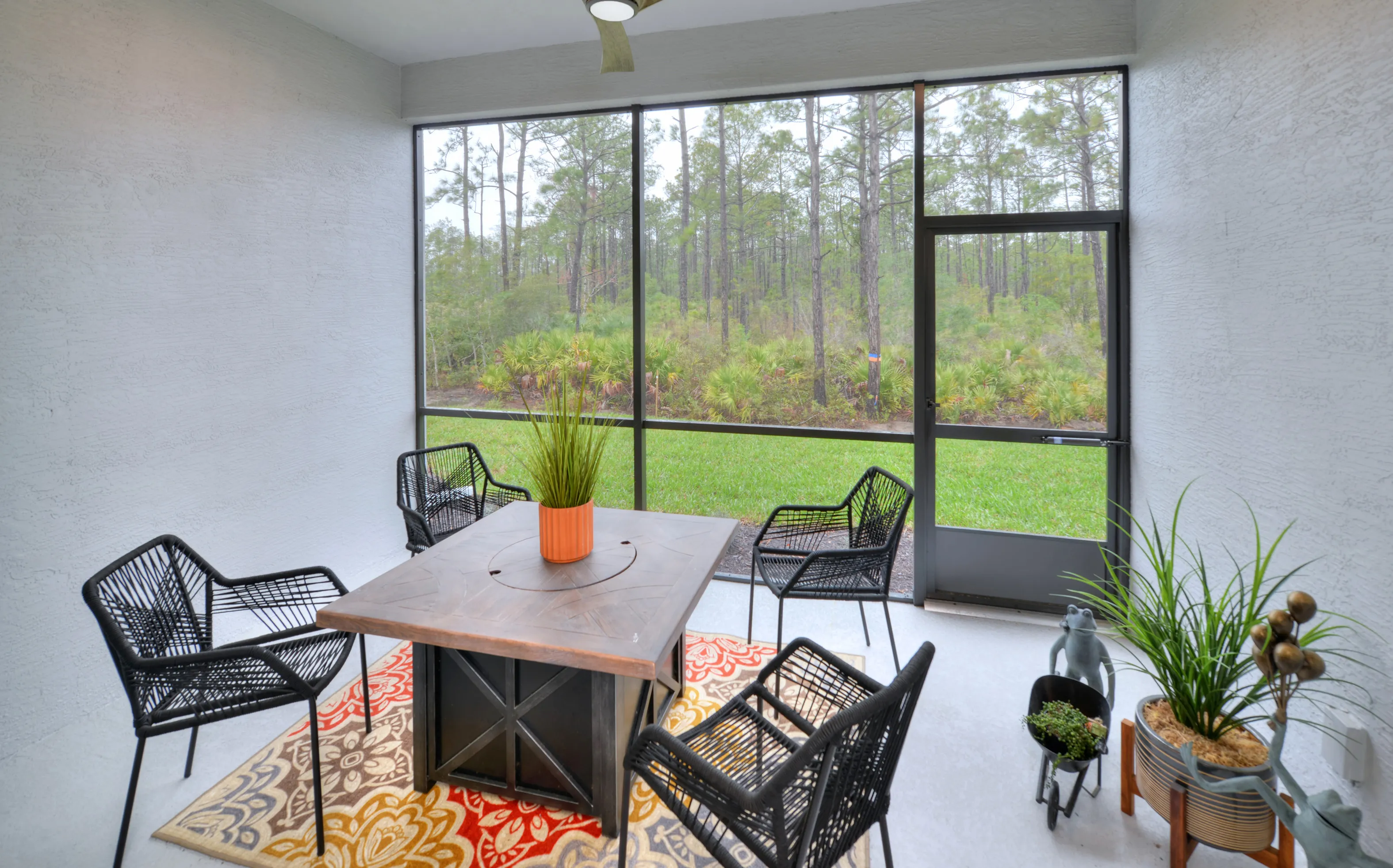 Screened-in patio at Woodhaven Townhomes with black wicker chairs, a square dining table, and a view of woods.