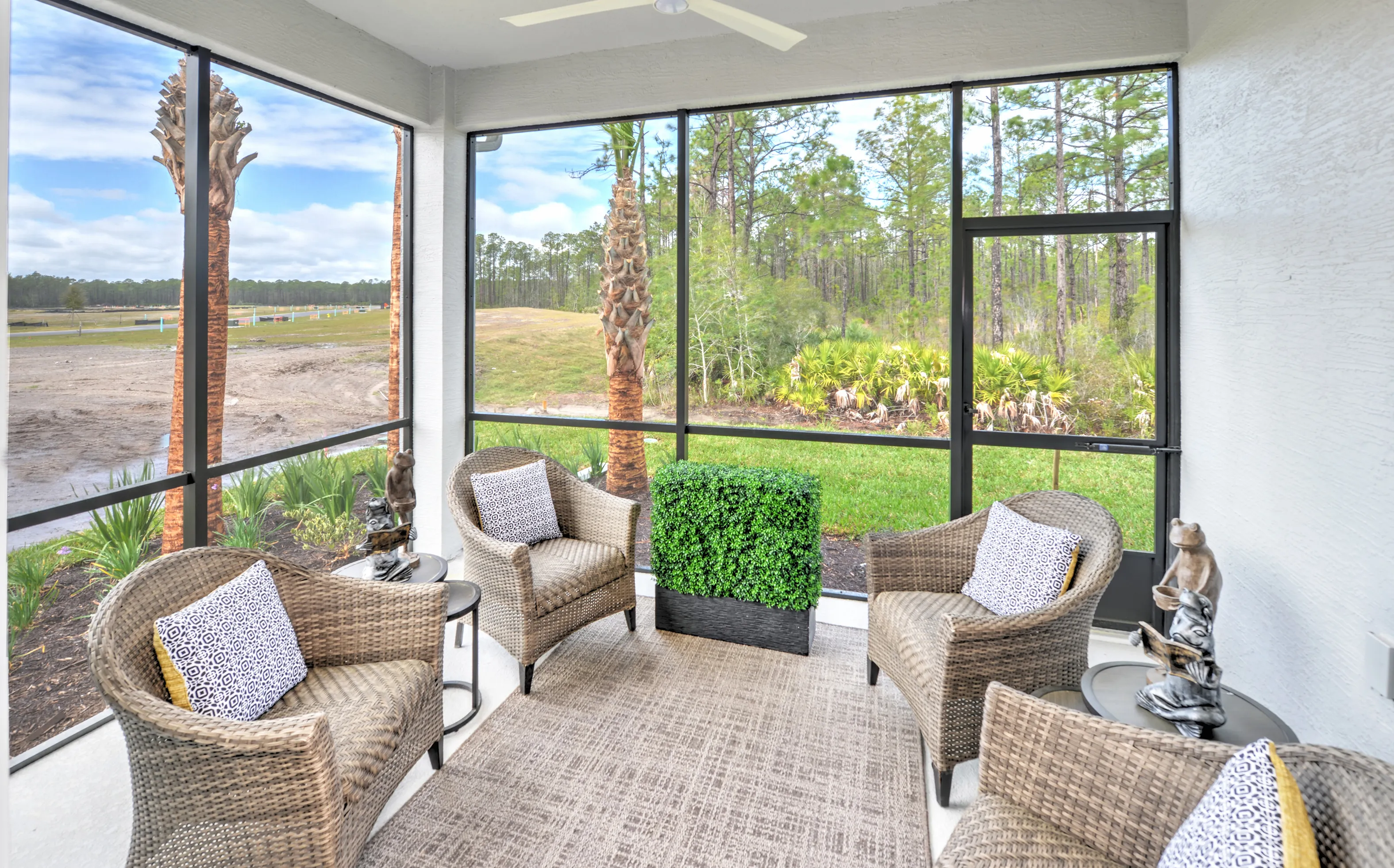 Screened-in patio at Woodhaven Townhomes with four wicker chairs, a central planter, and a view of trees and landscape.