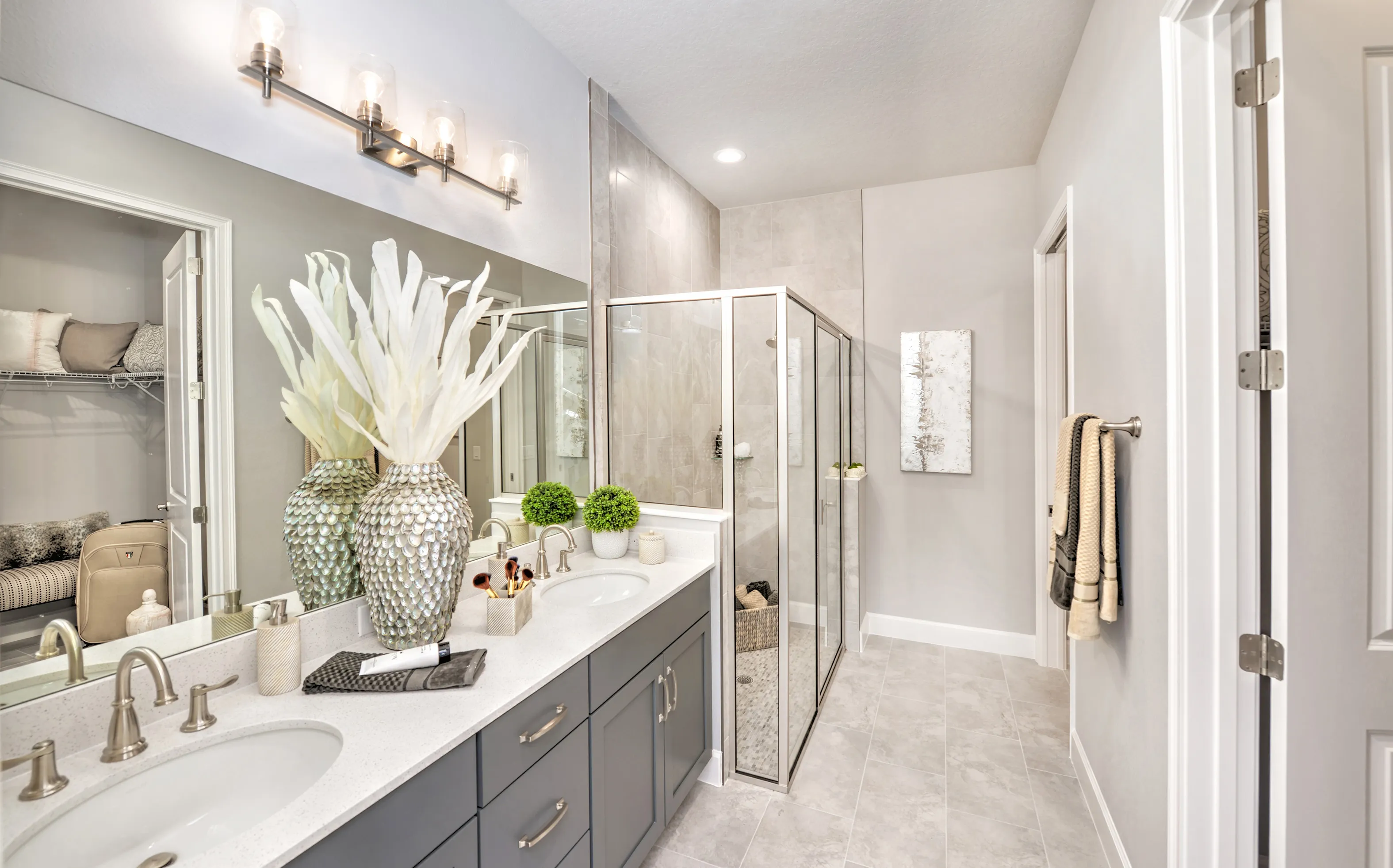 Modern bathroom in Woodhaven Townhomes featuring a dual-sink gray vanity, stone-look tile, and a glass-enclosed shower.