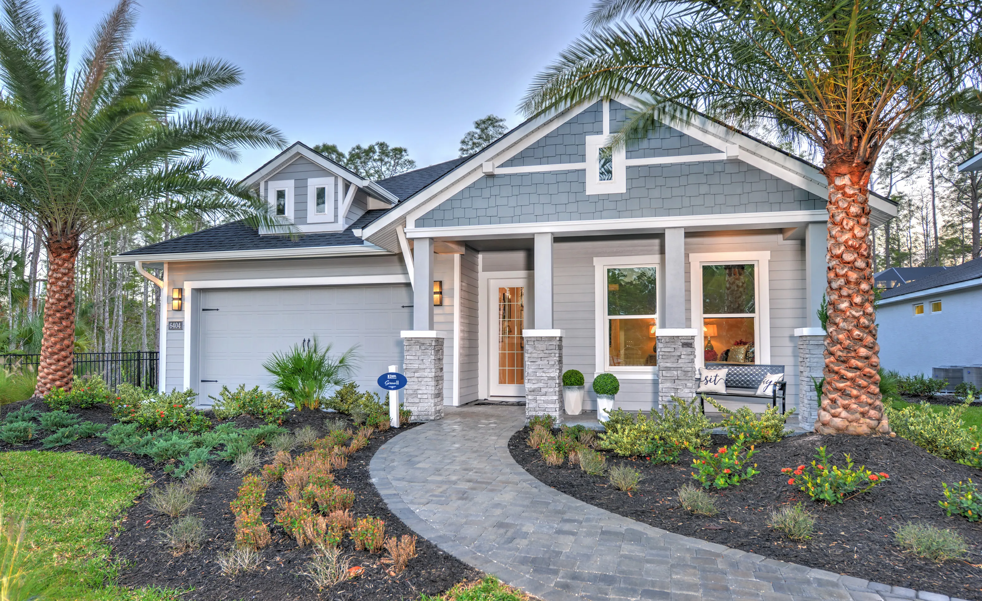Woodhaven Single Family home exterior with gray siding, stone porch pillars, a brick walkway, and two palm trees.