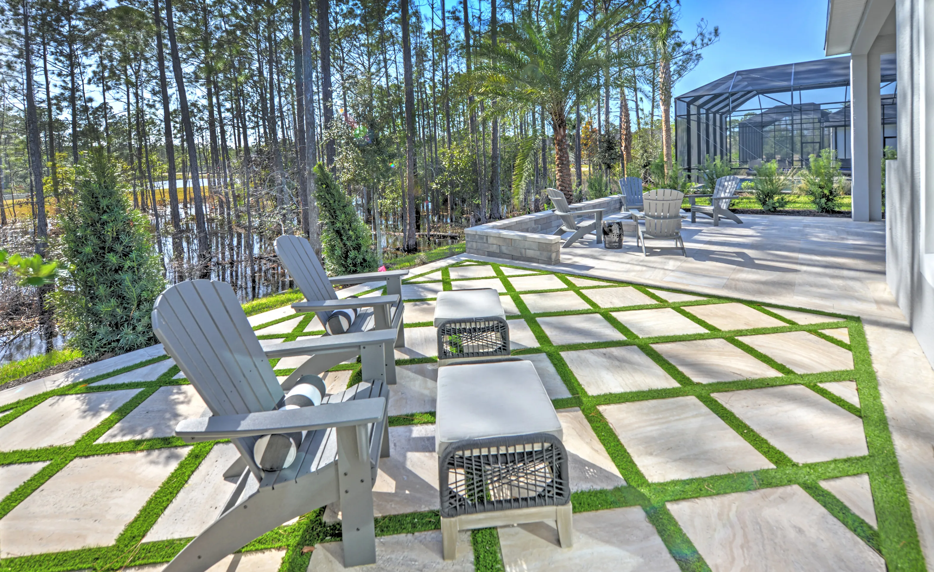 Outdoor patio at Woodhaven Single Family featuring stone pavers with grass inlay, adirondack chairs, and wooded views.