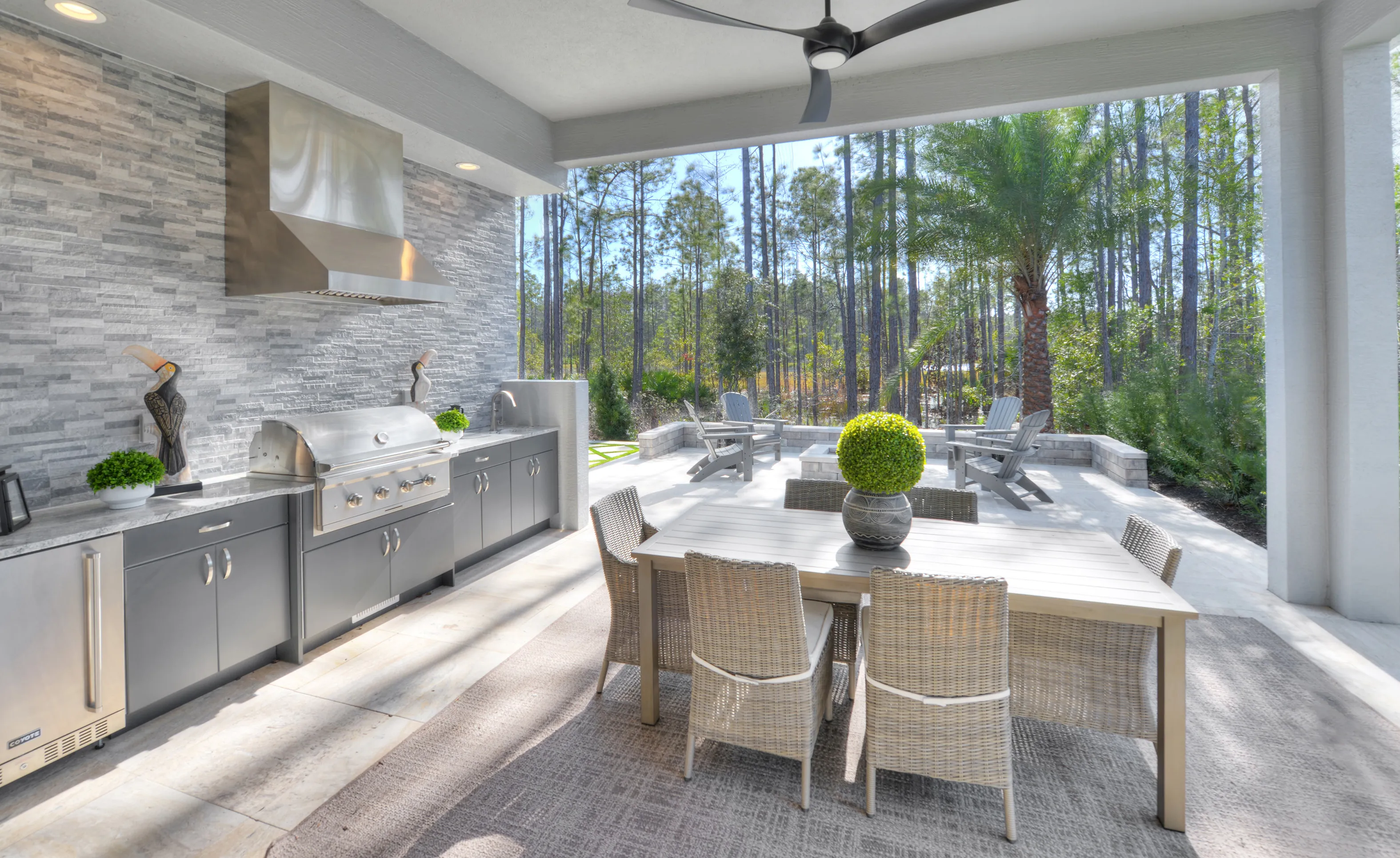 Covered outdoor kitchen and dining area at Woodhaven Single Family with a stone wall, grill, and patio furniture.