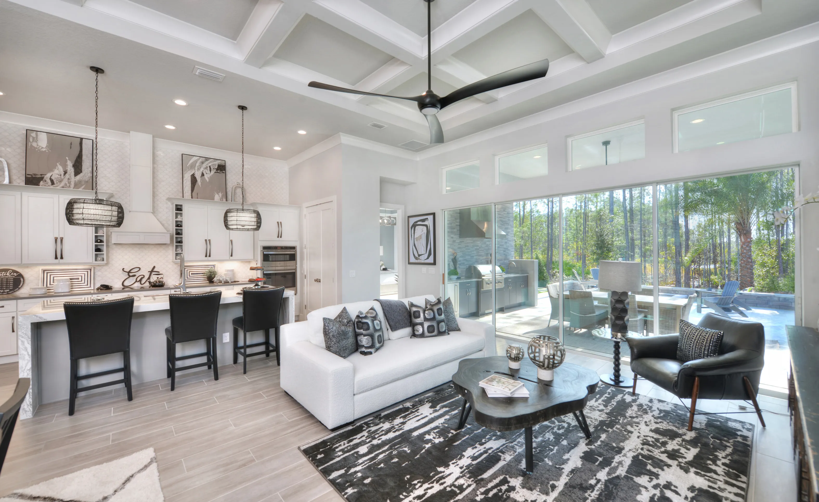 Open concept kitchen and living area with coffered ceiling, white cabinets, central island, and sliding glass patio doors.