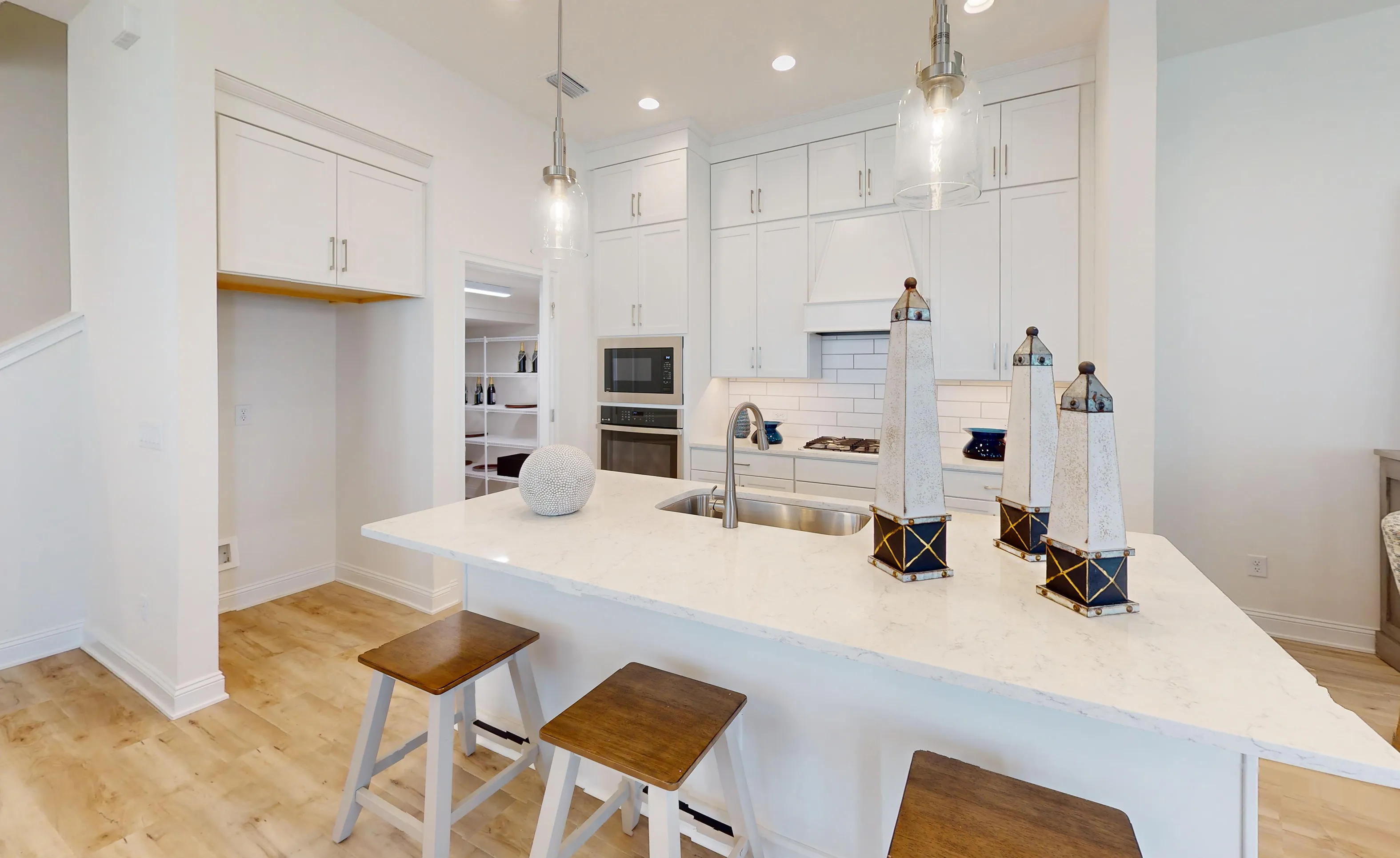 Kitchen in the Bartram B plan featuring white cabinets, a stone island with sink, and a walk-in pantry.