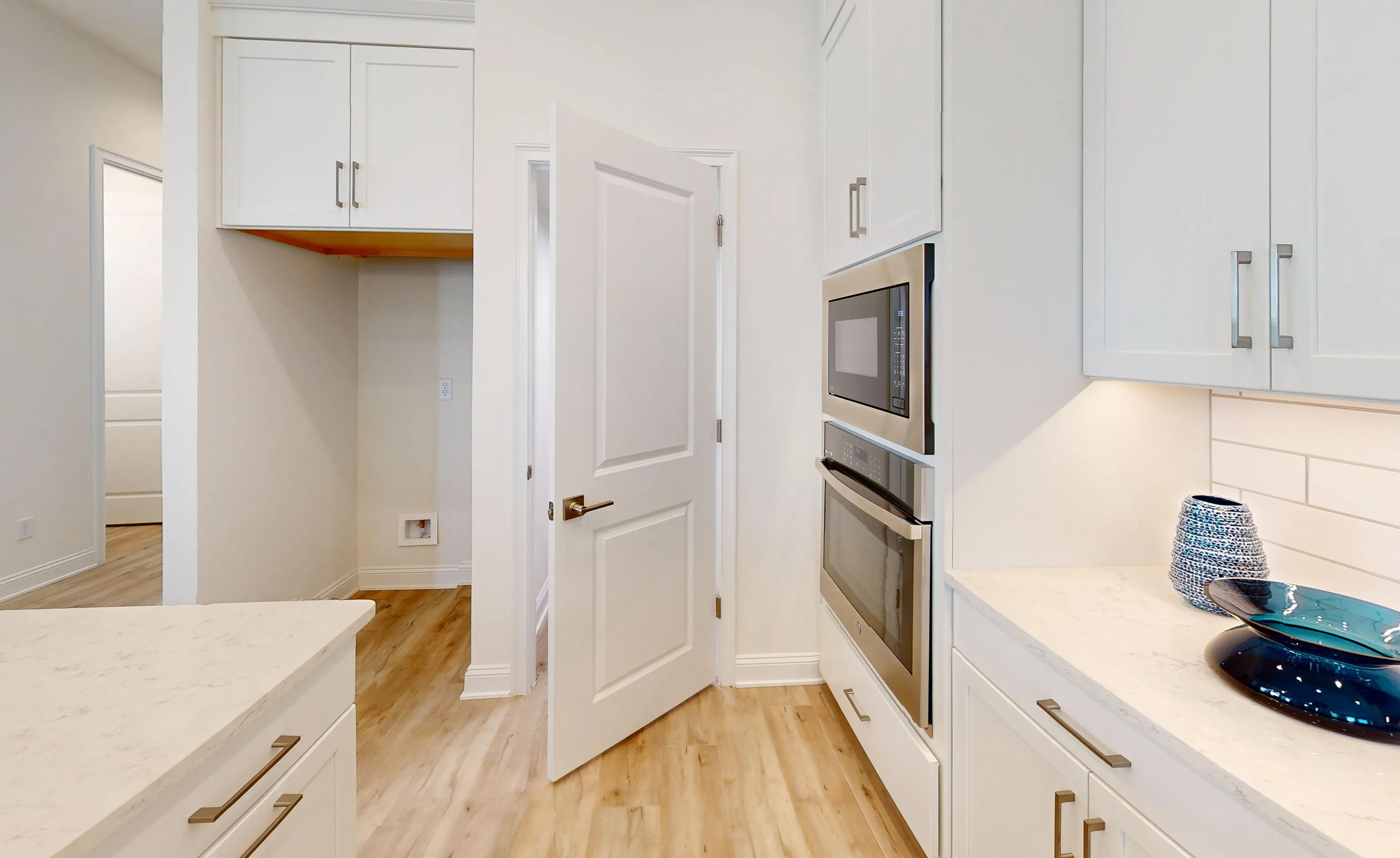 Laundry room featuring white cabinetry, light wood-look flooring, stainless steel wall oven, and a built-in microwave.