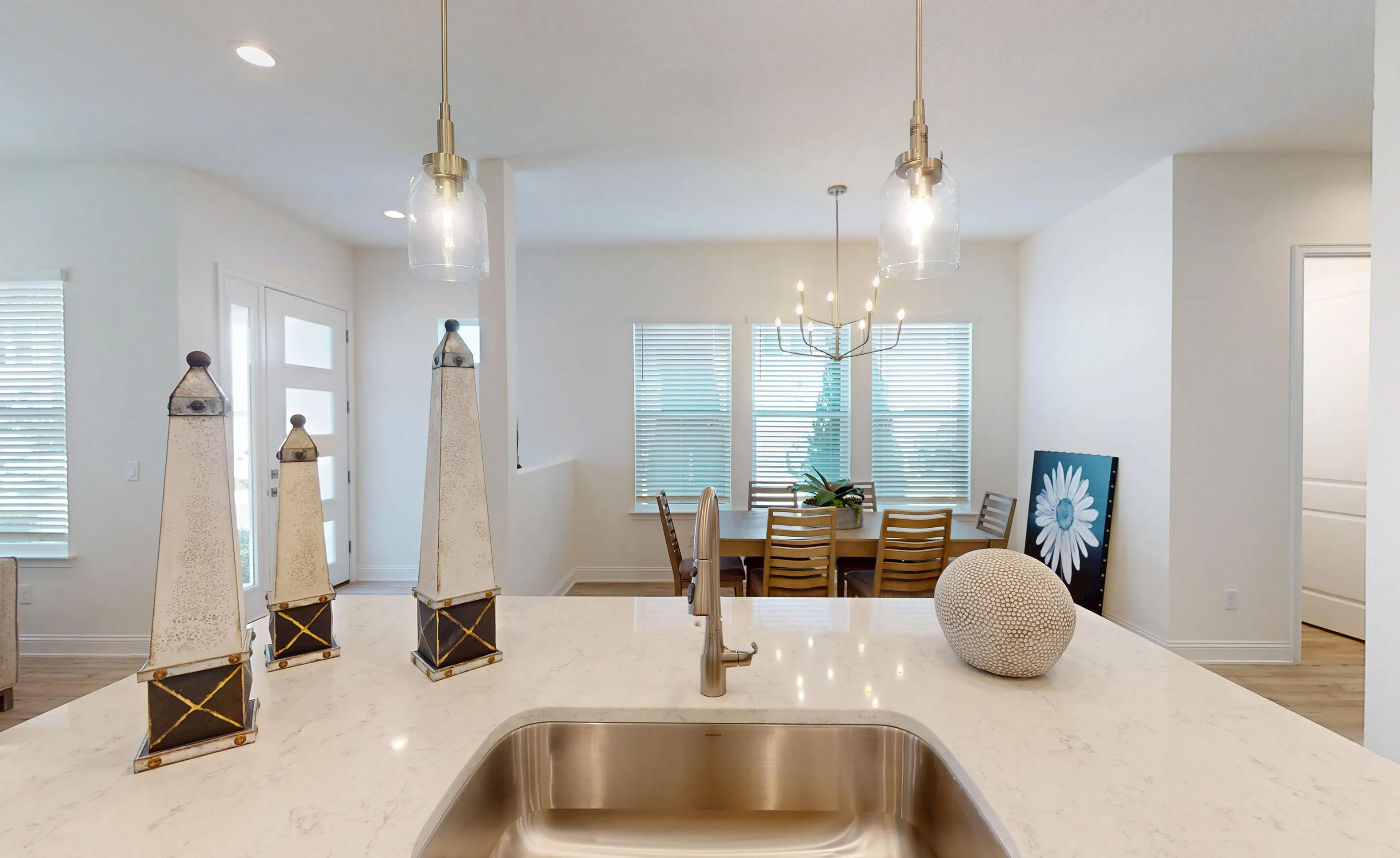 Kitchen island with white marble-look countertop and steel sink, overlooking an open dining area with a modern chandelier.