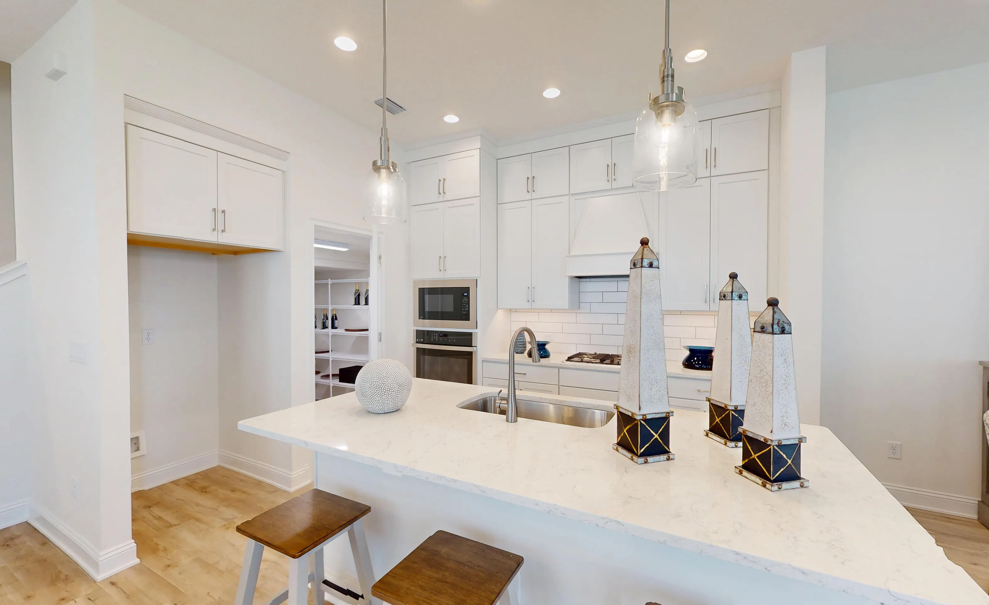 Kitchen with white cabinets, light countertops, a central island with sink, and a walk-in pantry in the Bartram B plan.
