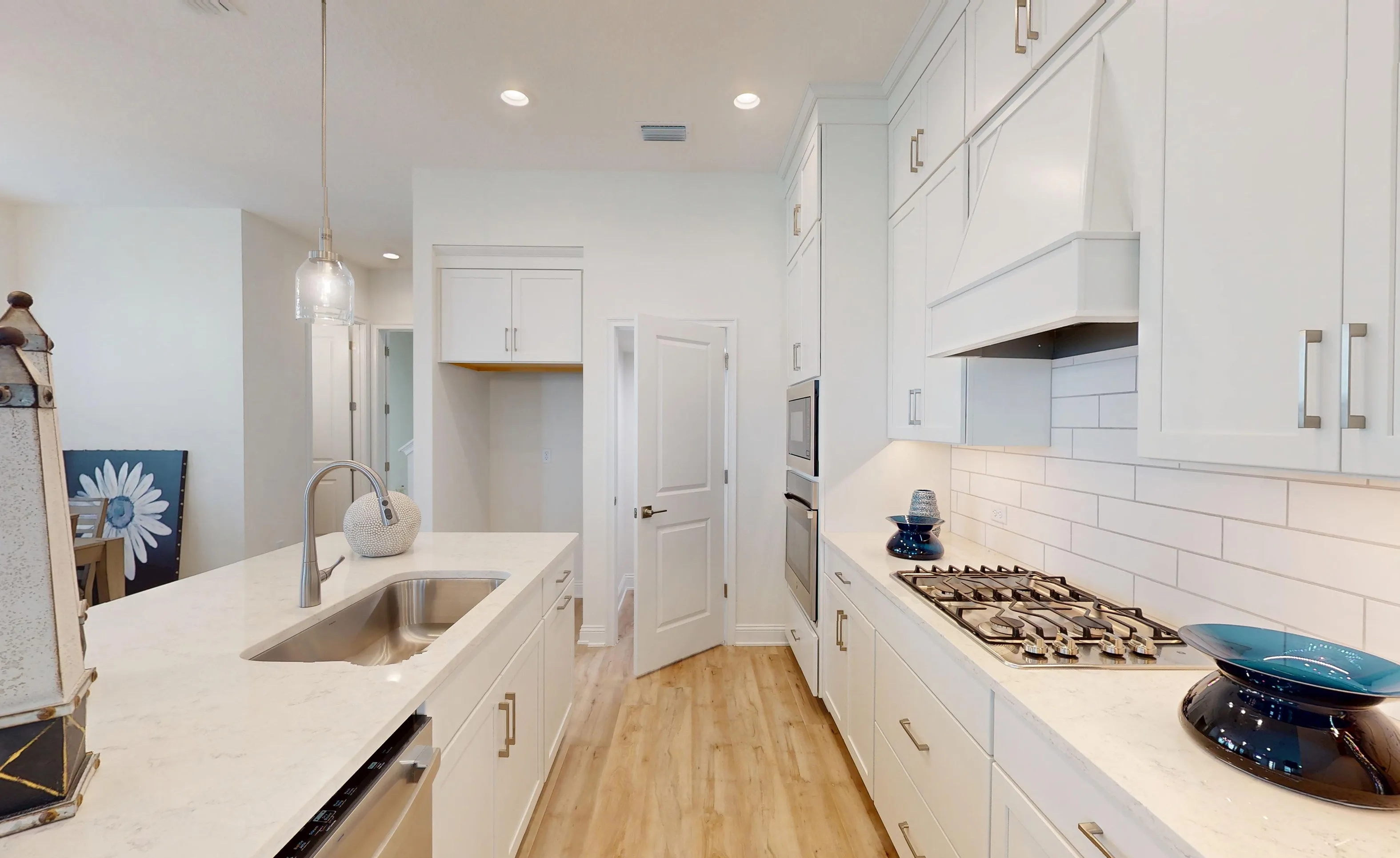 Kitchen with white cabinets, quartz countertops, white subway tile backsplash, gas cooktop, and a central island sink.