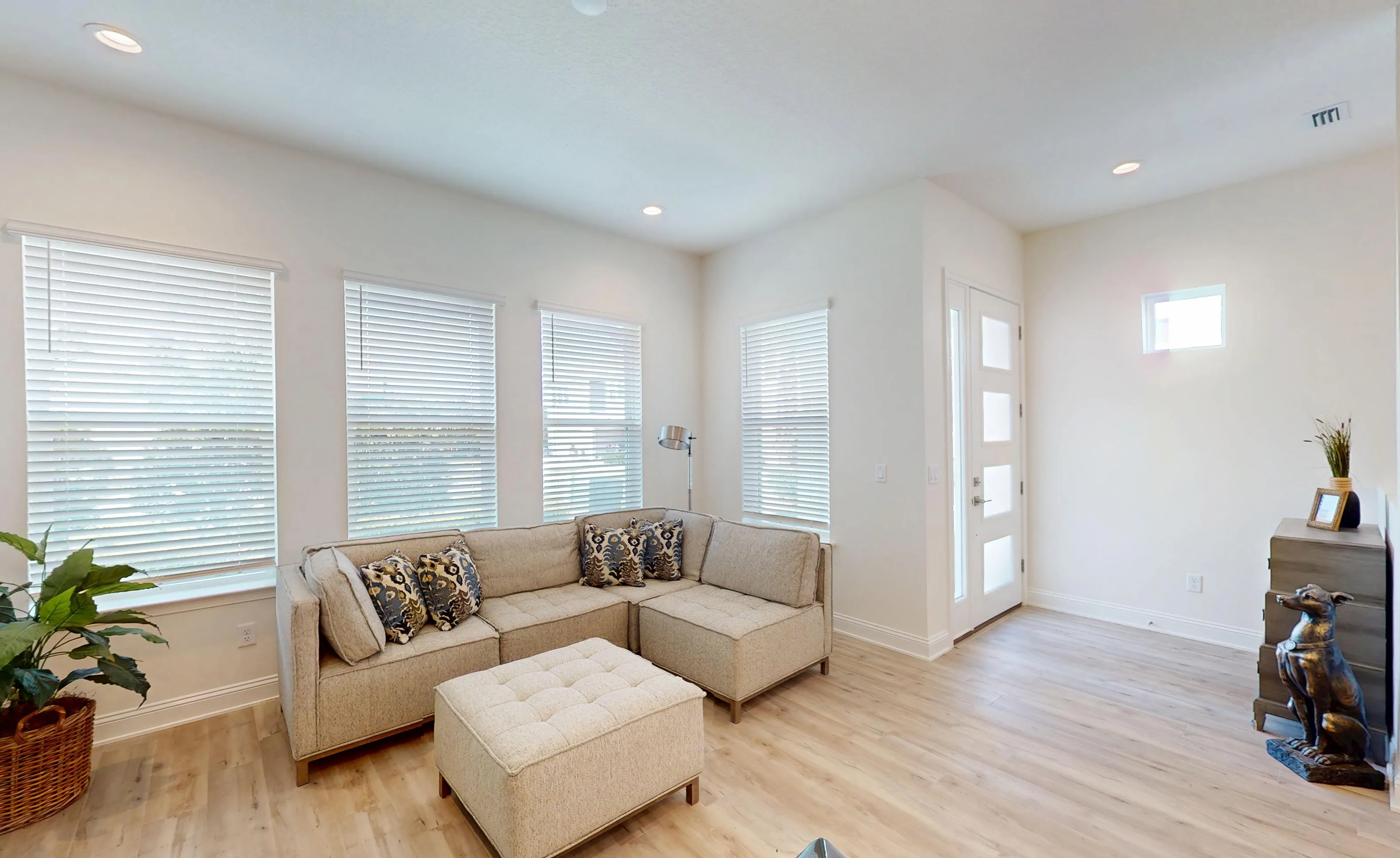 Living room in the Bartram floor plan with light wood floors, a beige sectional sofa, and a white door with glass panels.
