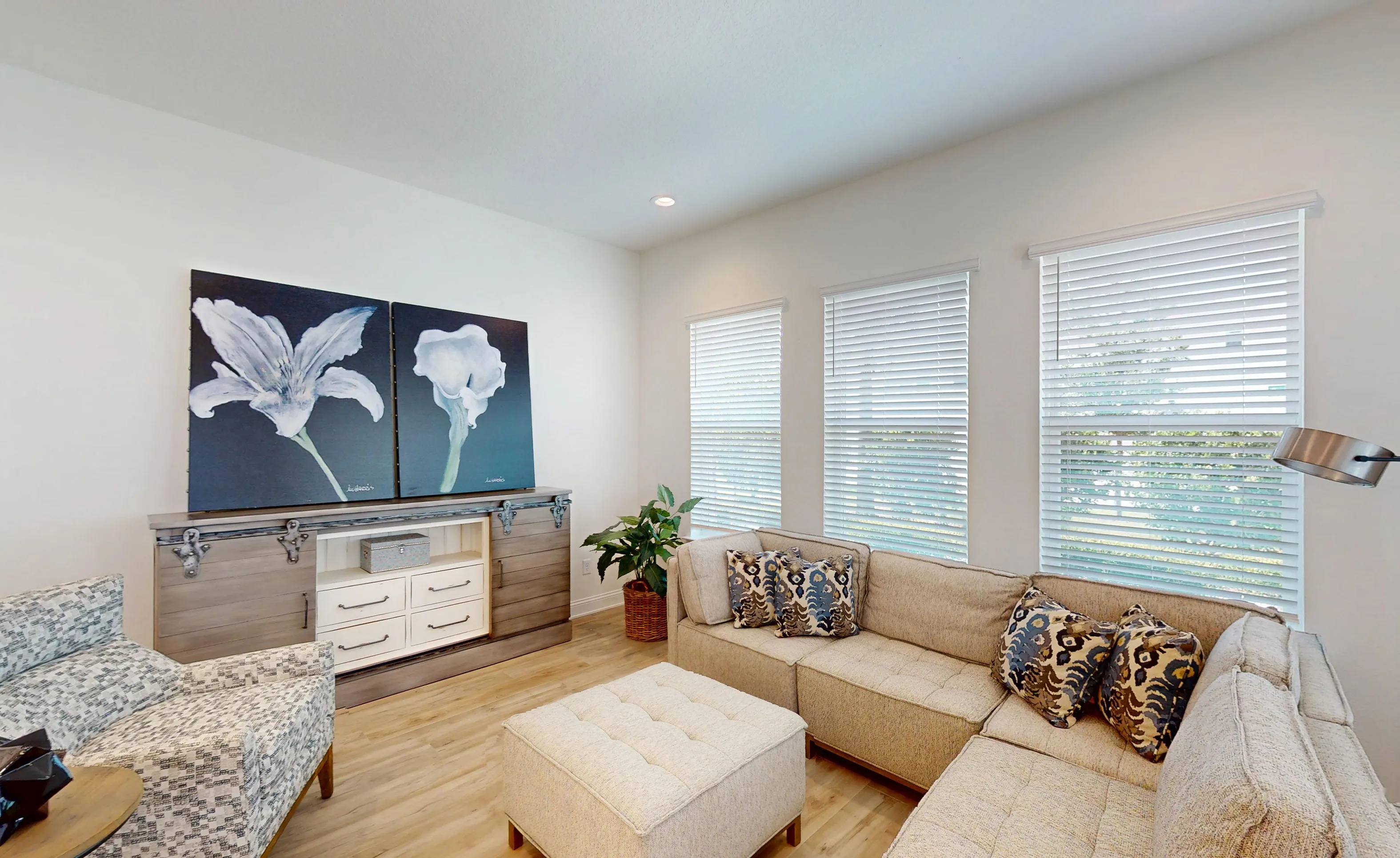 Living room in the Bartram B plan featuring light wood-look flooring, a sectional sofa, and a rustic console with sliding doors.
