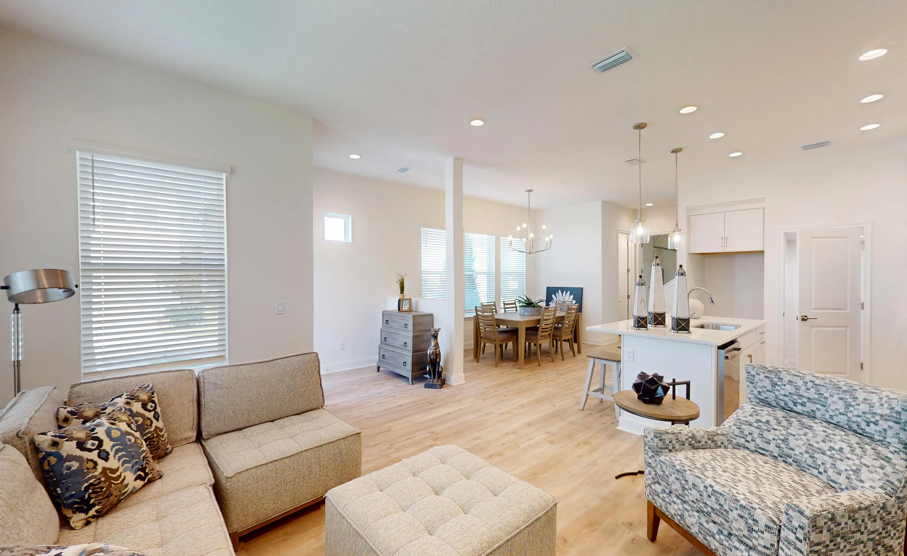 Living room of the Bartram B plan featuring light wood flooring, an open floor plan to the dining area, and a kitchen.