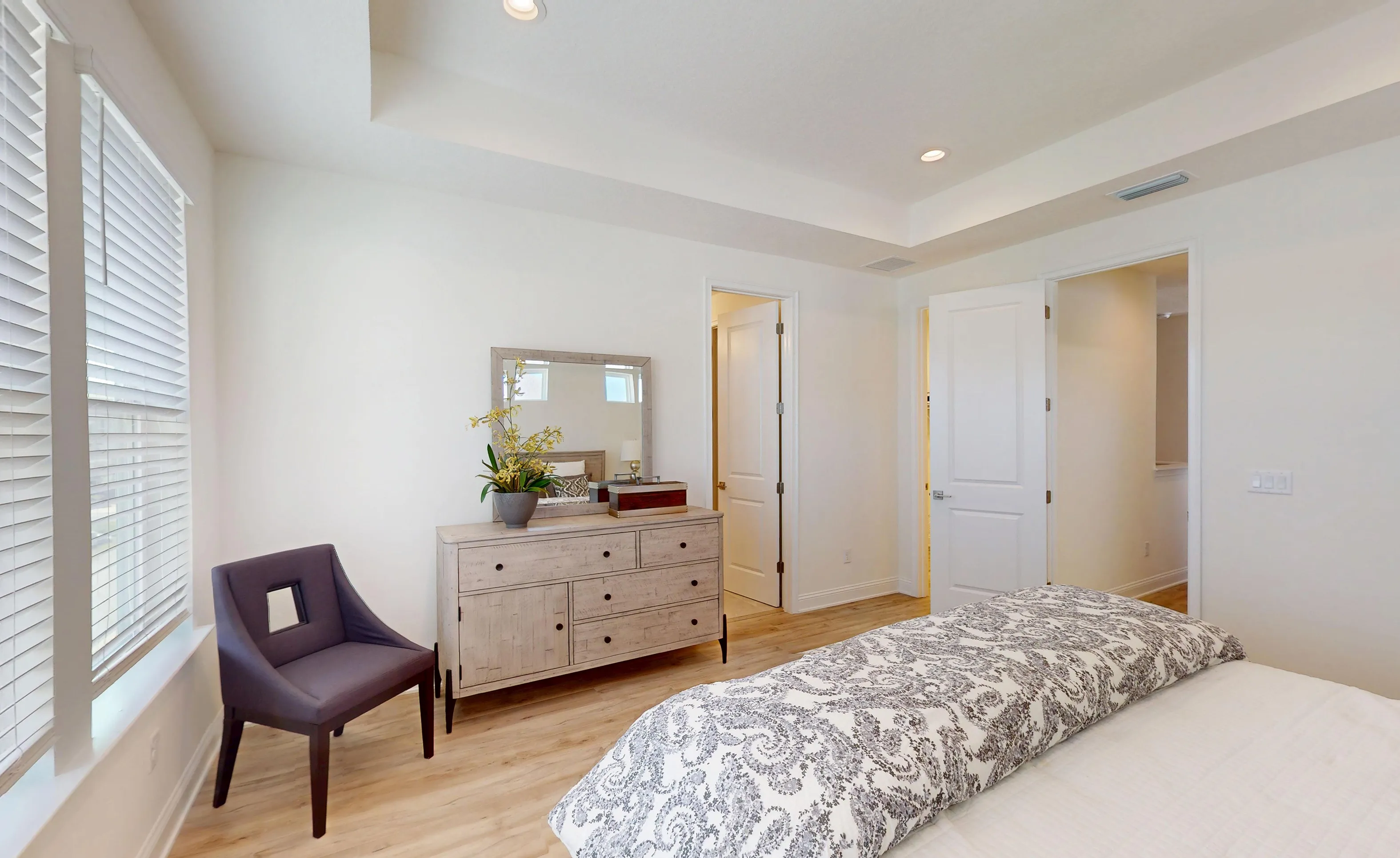 Primary bedroom in the Bartram plan featuring white walls, wood-look flooring, a tray ceiling, and two interior doorways.