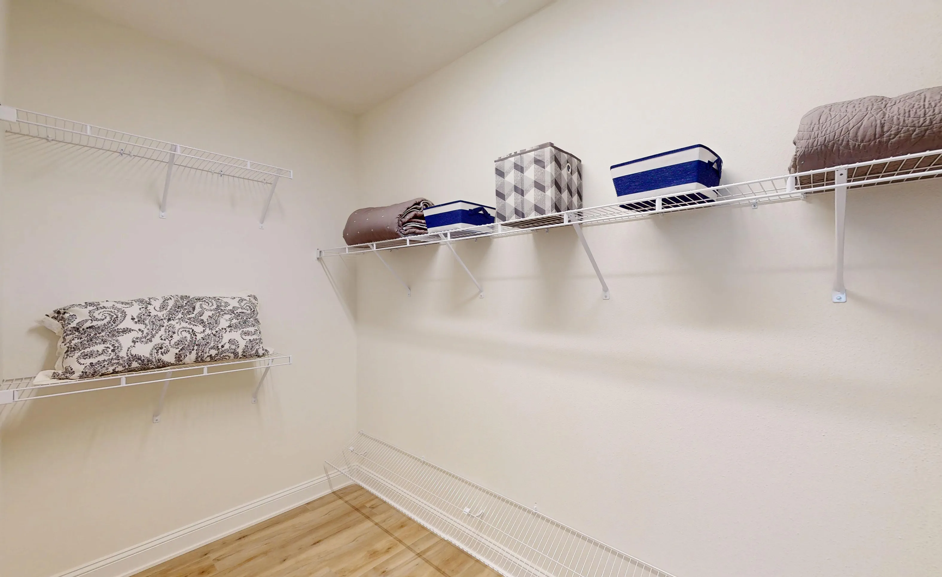Walk-in closet with white wire shelving, wood-look flooring, and neutral walls in the Bartram - B plan.