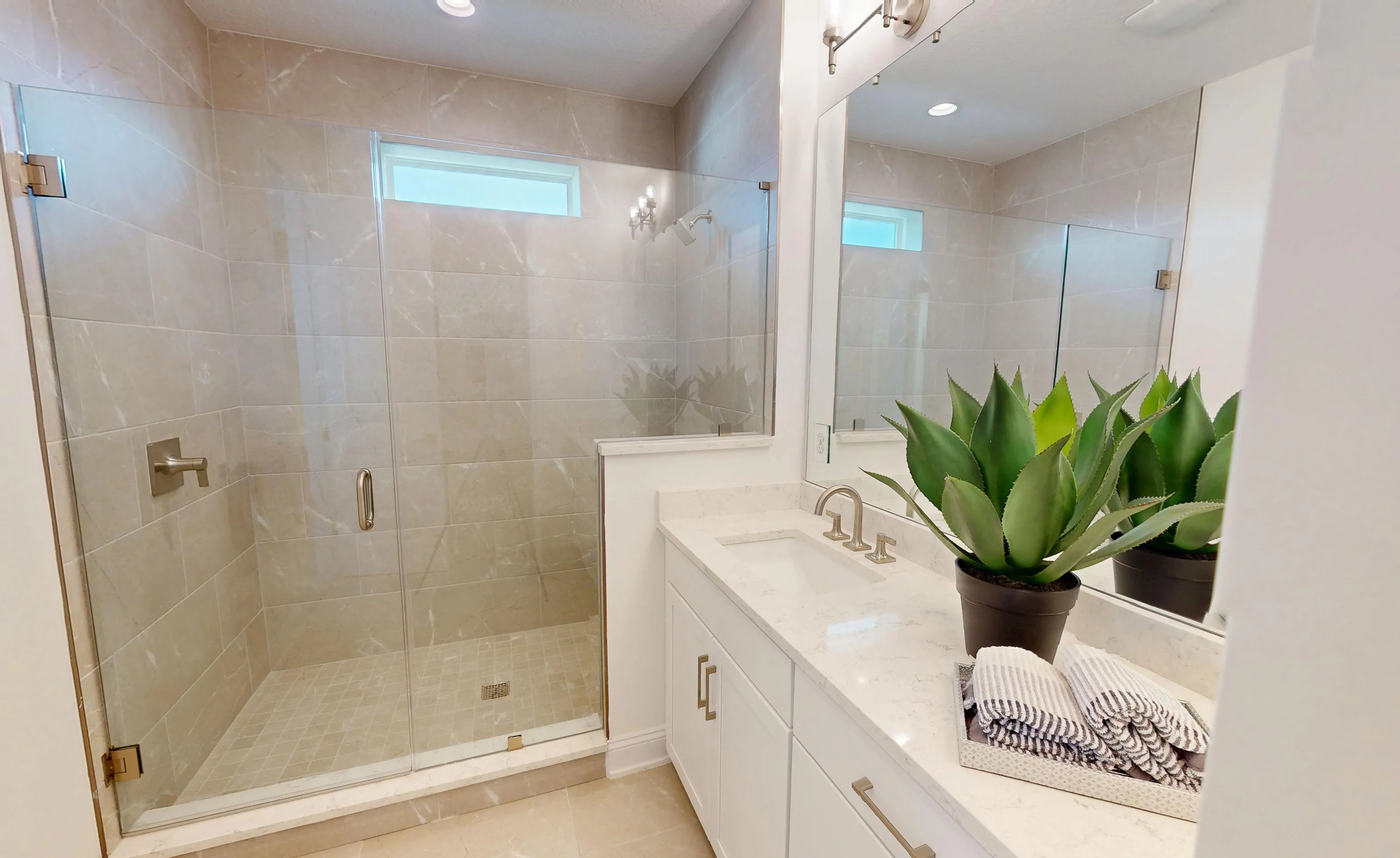 Secondary bathroom with glass-enclosed walk-in shower, light-toned tile, white vanity, and a large mirror.