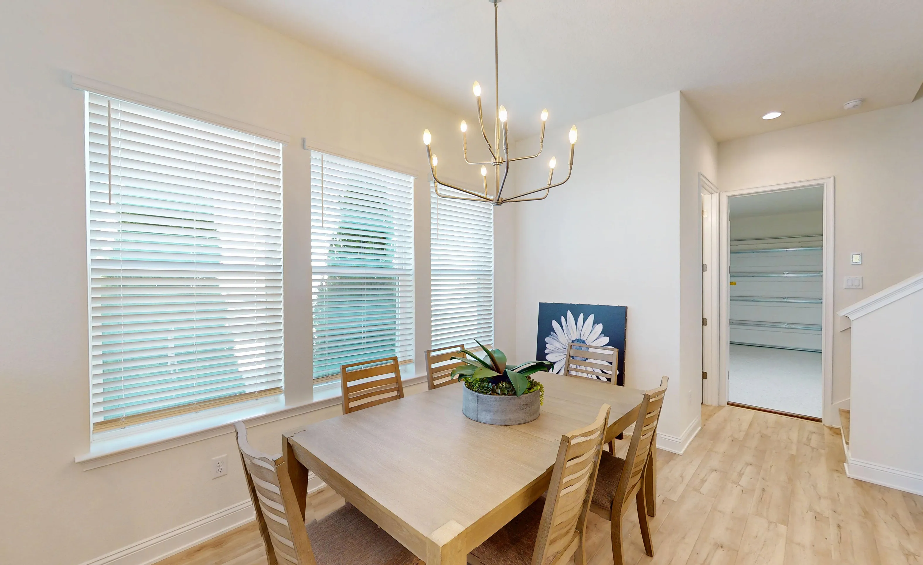 Dining room in the Bartram plan featuring a wooden table with chairs, a modern chandelier, and large windows with blinds.