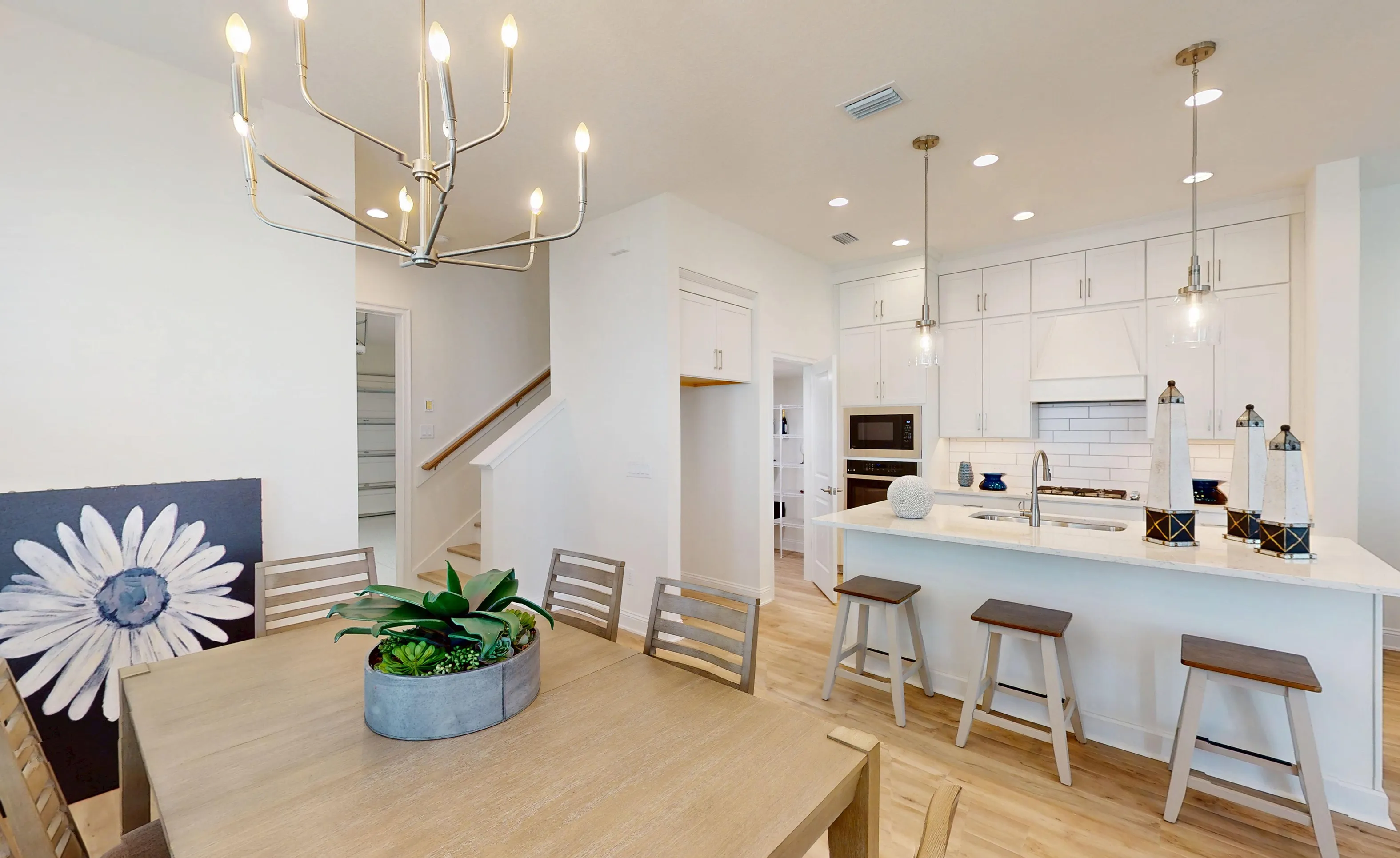 Kitchen of the Bartram-B plan in Nocatee featuring white cabinetry, a center island with bar stools, and a dining area.