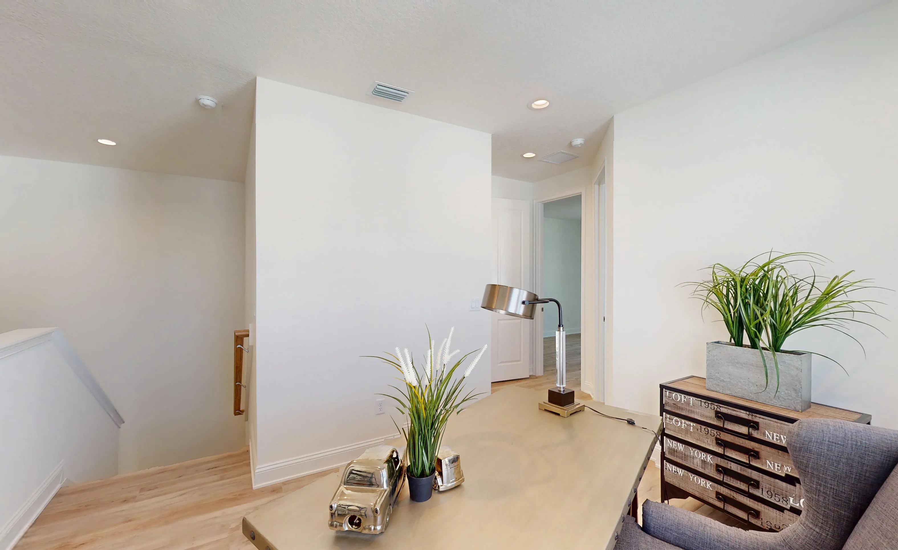 Home office in the Bartram B plan featuring a desk, decorative accents, and a view toward an open hallway and staircase.