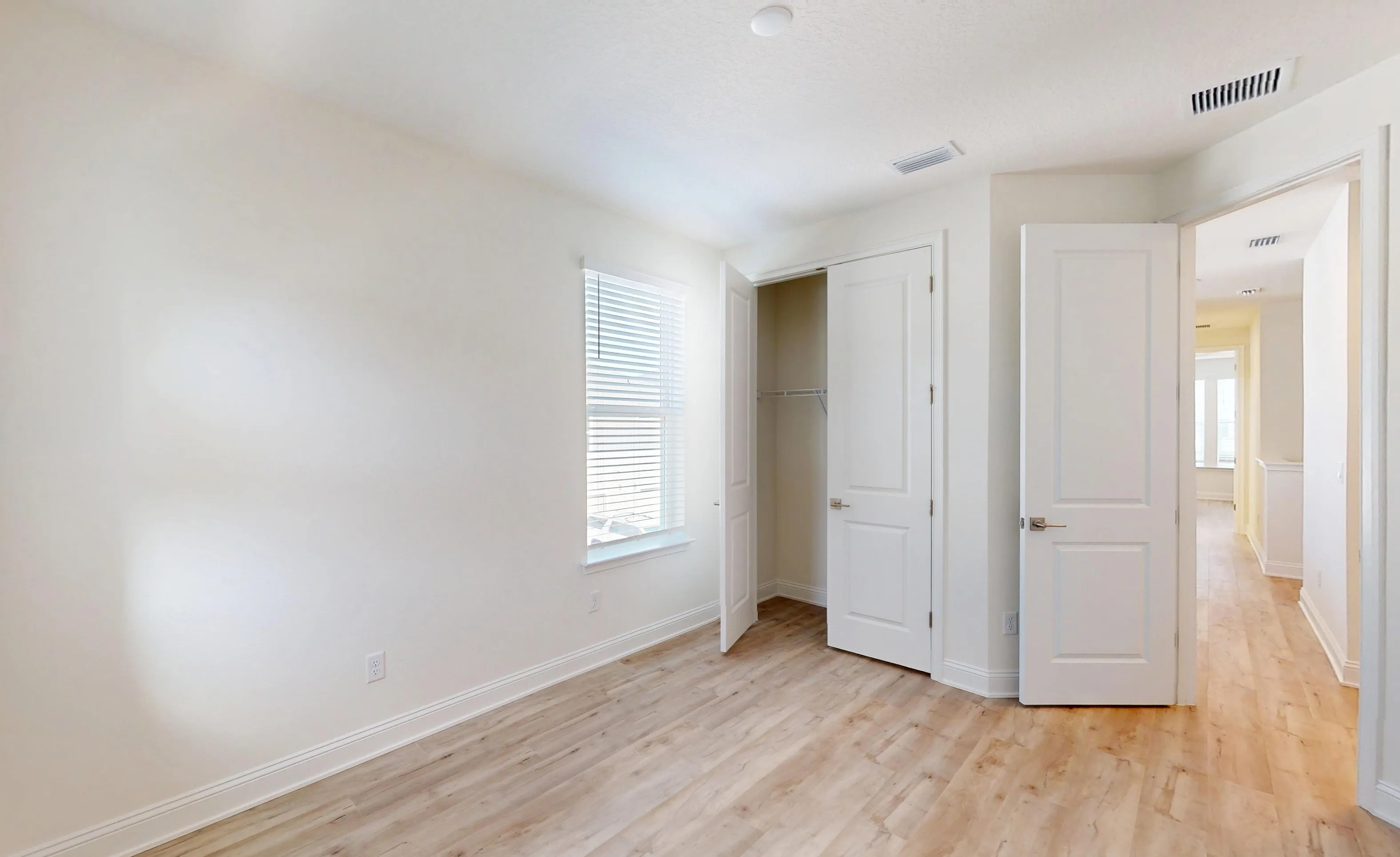 Secondary bedroom with light wood-look flooring, white walls, a window with blinds, and an open reach-in closet.