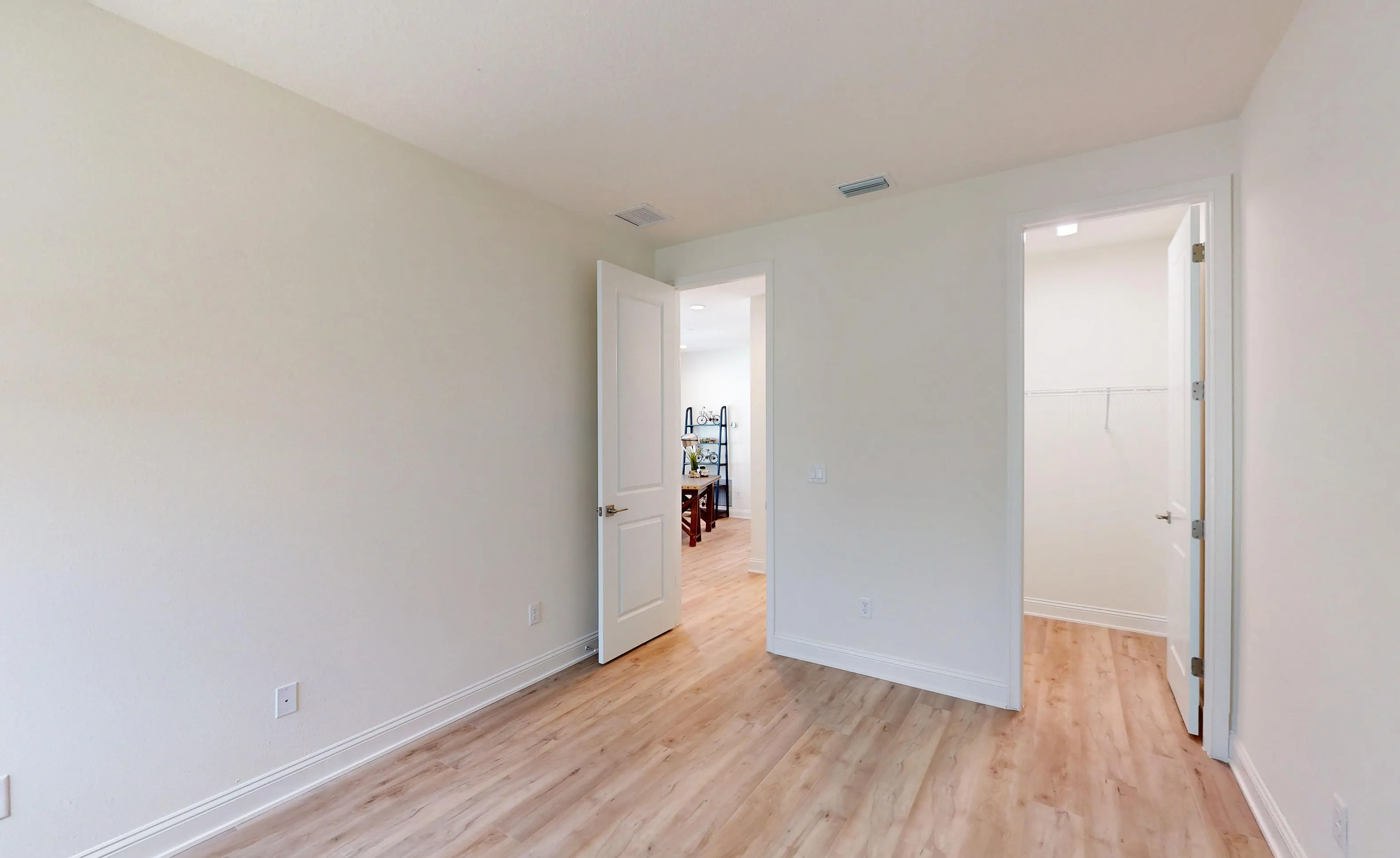 Secondary bedroom in the Bartram floor plan with light wood-look flooring, white walls, an open doorway, and a walk-in closet.