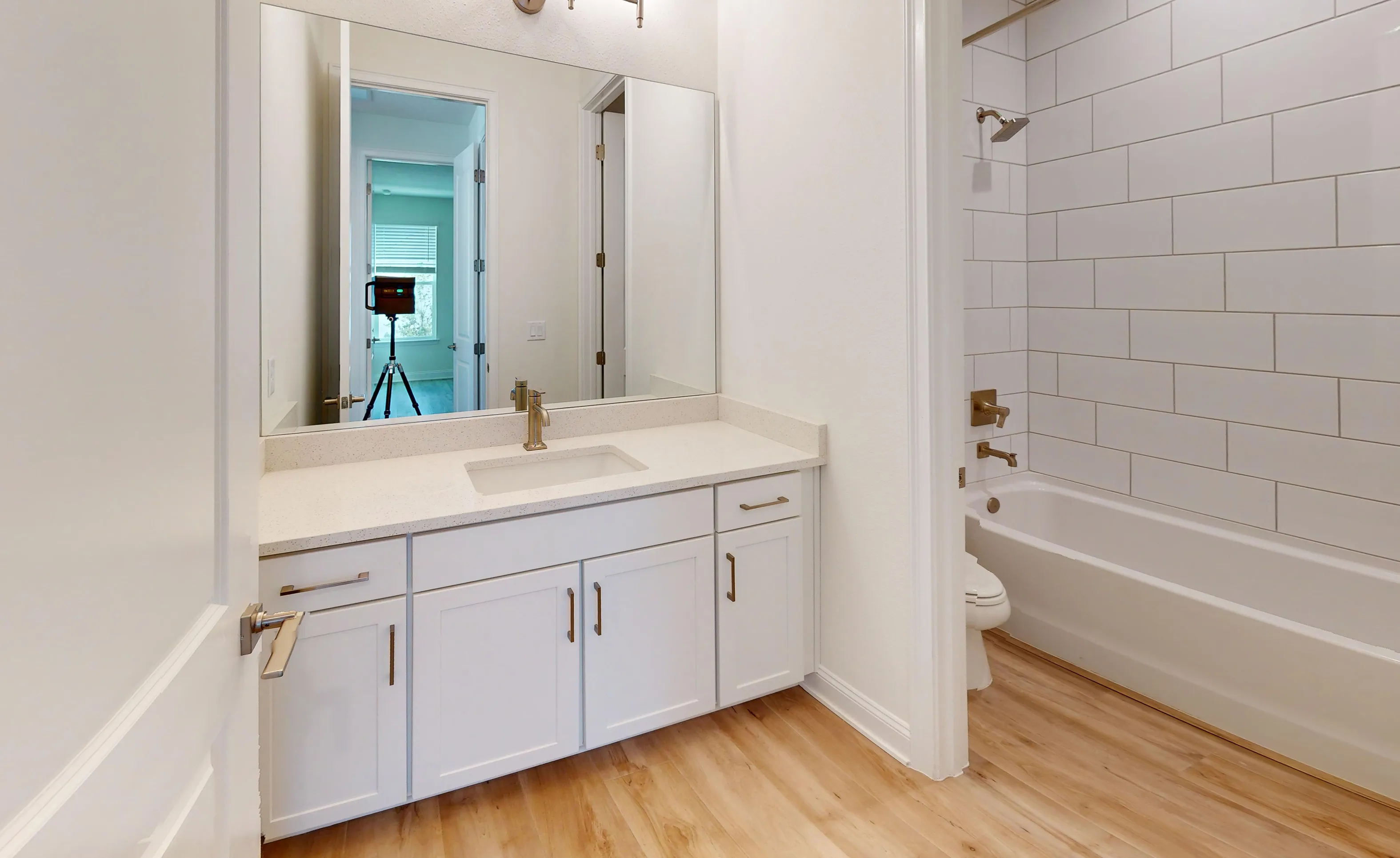 Secondary bathroom with white vanity, solid surface countertop, large mirror, and tub-shower combo with white subway tile.