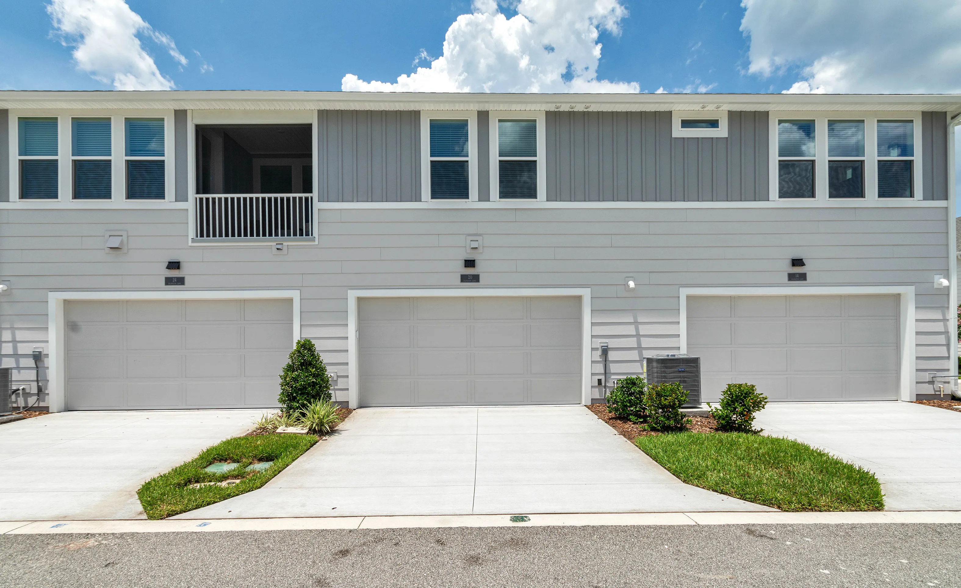 Rear exterior view of Castillo townhome in Nocatee featuring light gray siding, three garage doors, and a screened balcony.